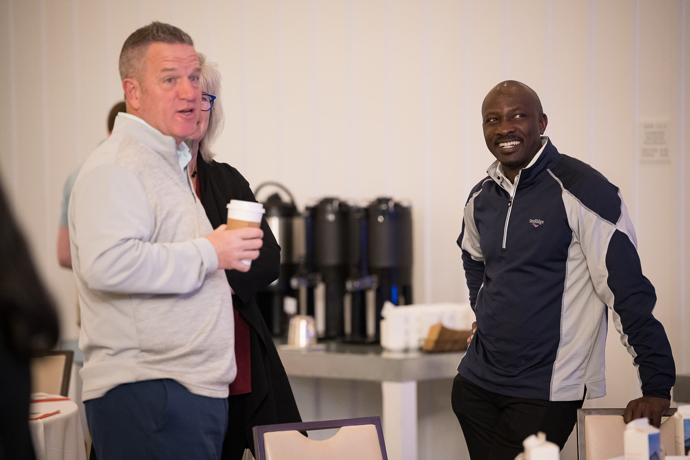 Two guests talking beside the coffee urns at a hosted morning session