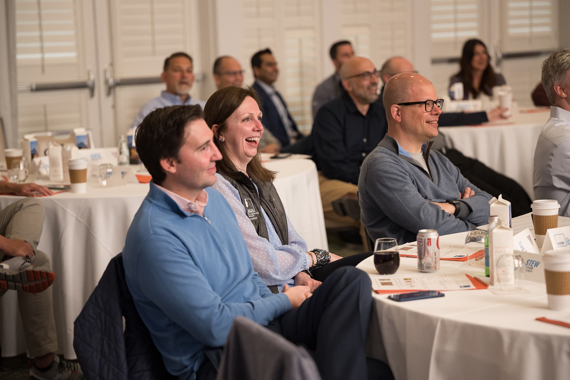 Guests at round tables laughing during remarks at a hosted morning session