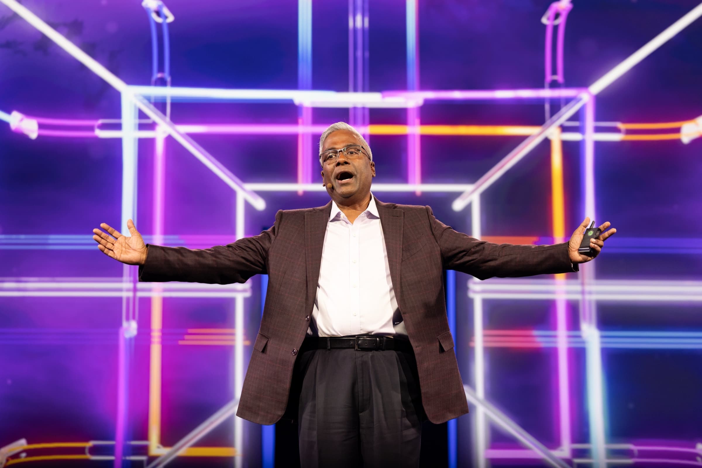 Keynote speaker with arms wide open in front of an illuminated geometric stage structure