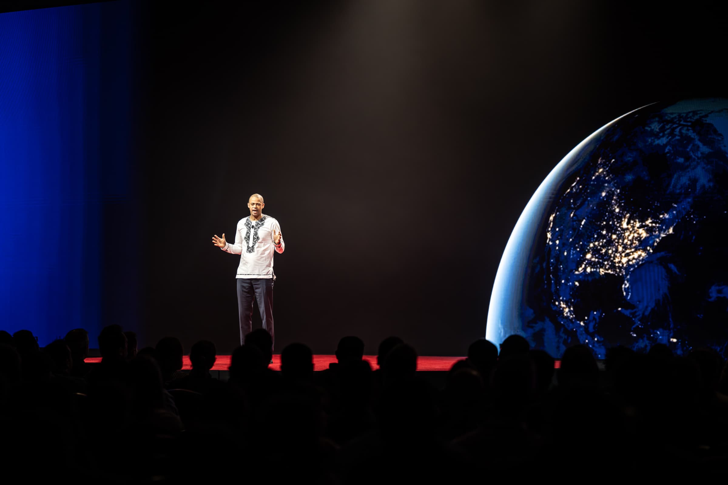 Keynote speaker alone on a dark stage in front of a large illuminated screen