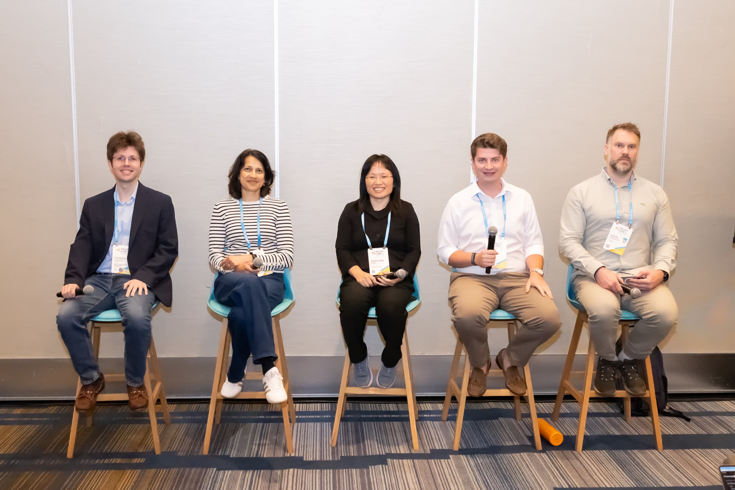 Five panelists seated on stools during a conference session