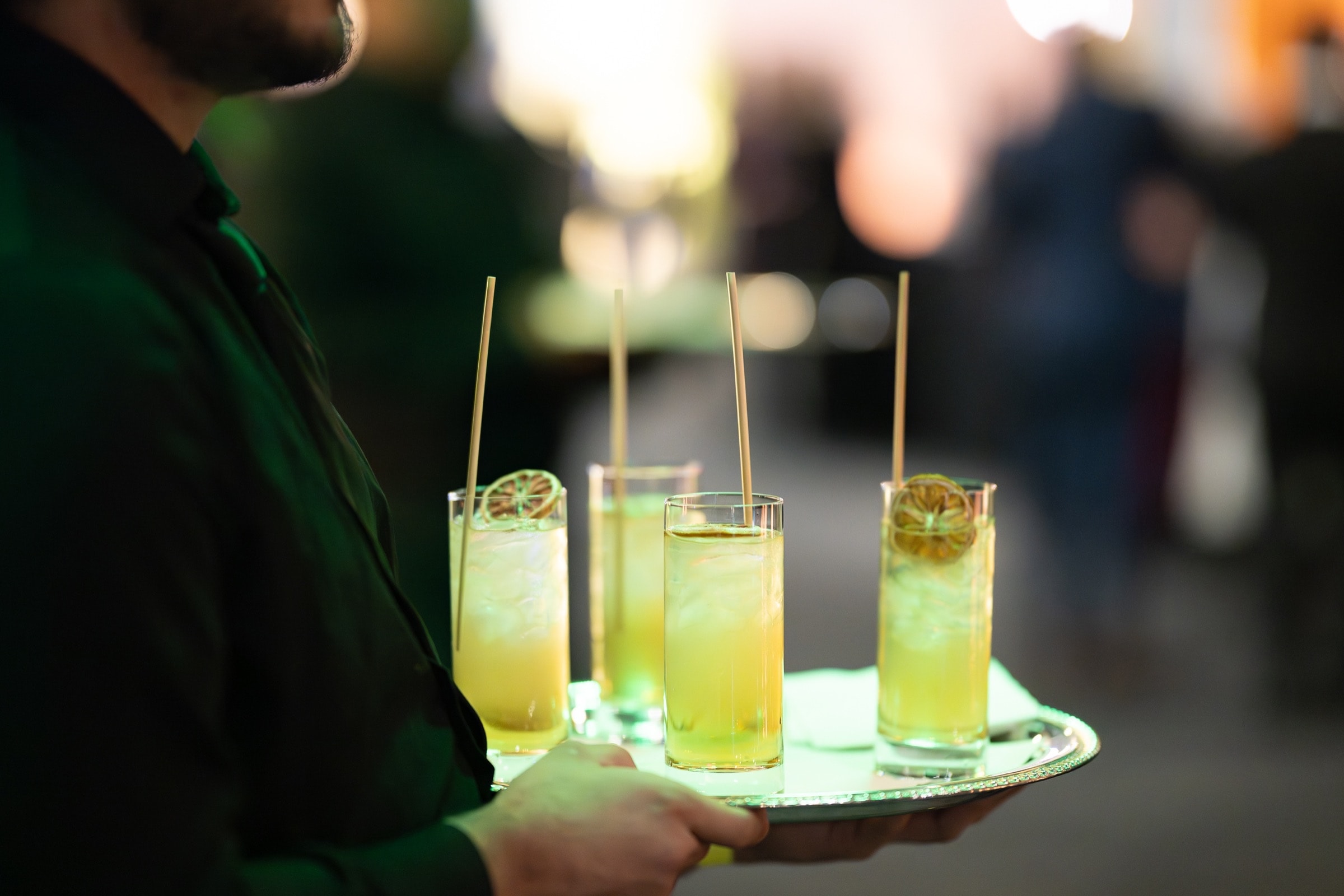 Server carrying a tray of garnished cocktails through an evening reception