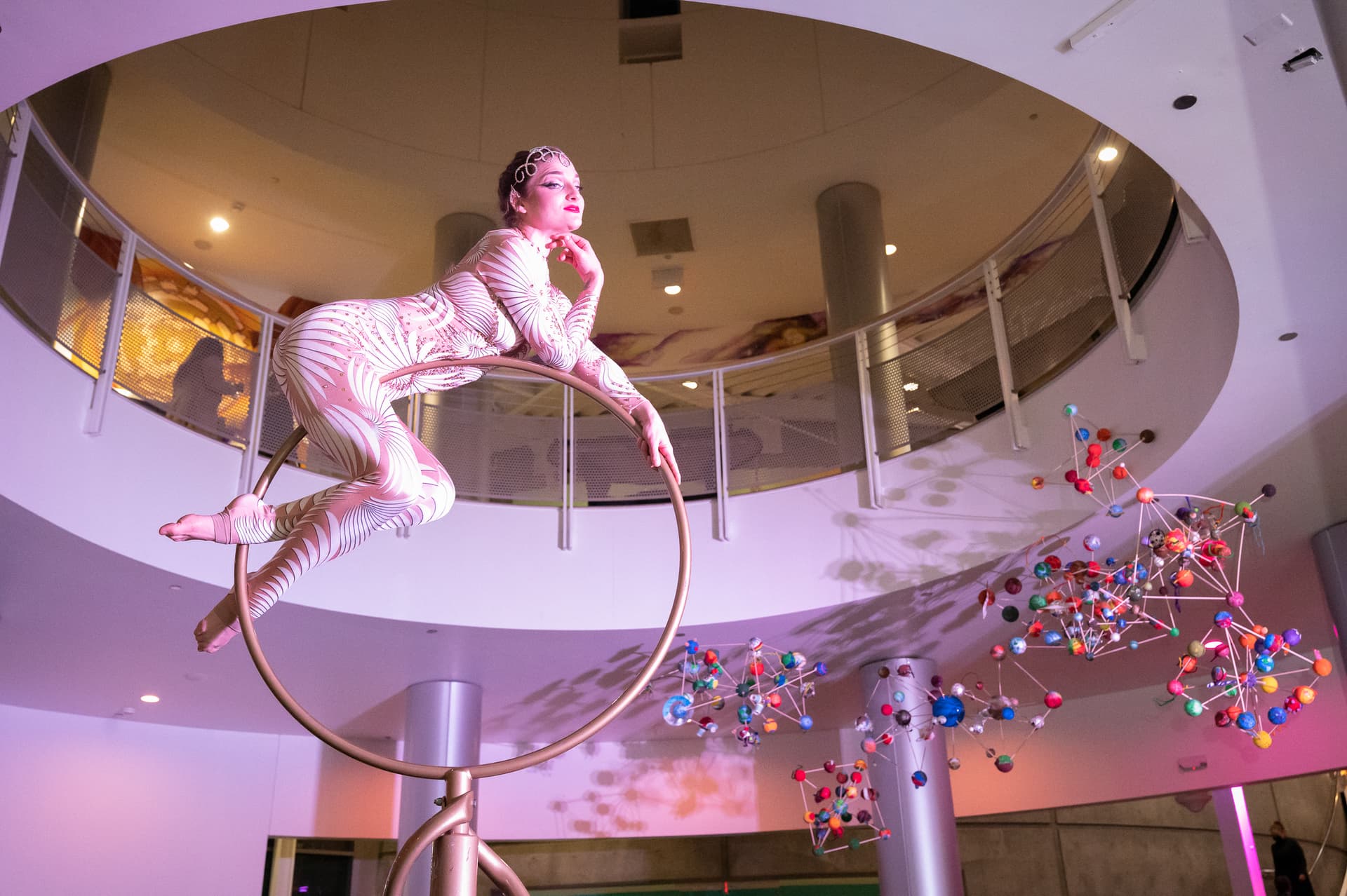 Aerial performer posed on a suspended ring in a modern atrium