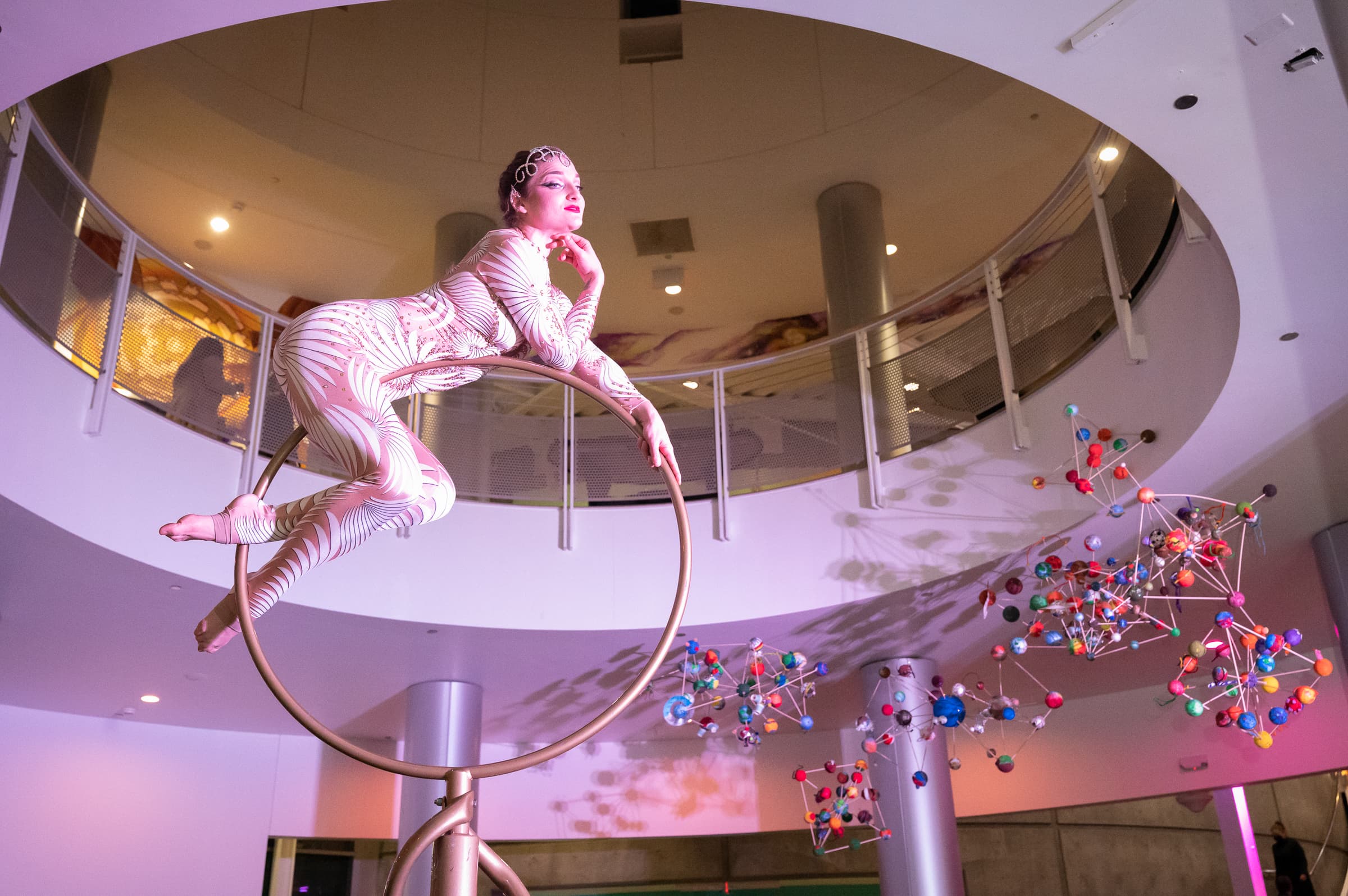 Aerial performer posed on a suspended ring in a modern atrium