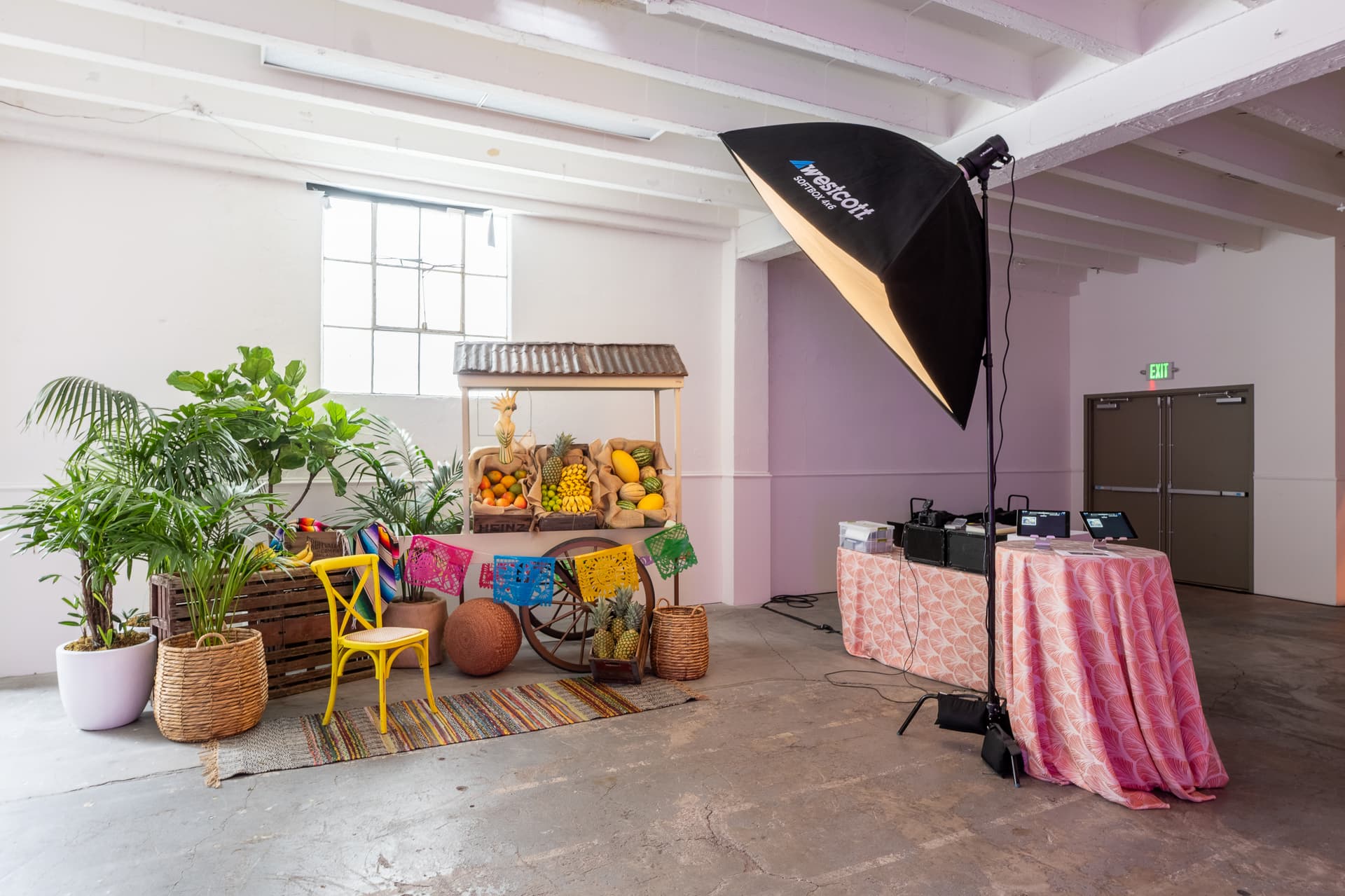 Creative studio setup featuring colorful decorative fruits, baskets, bright yellow chairs, and professional lighting against a white wall