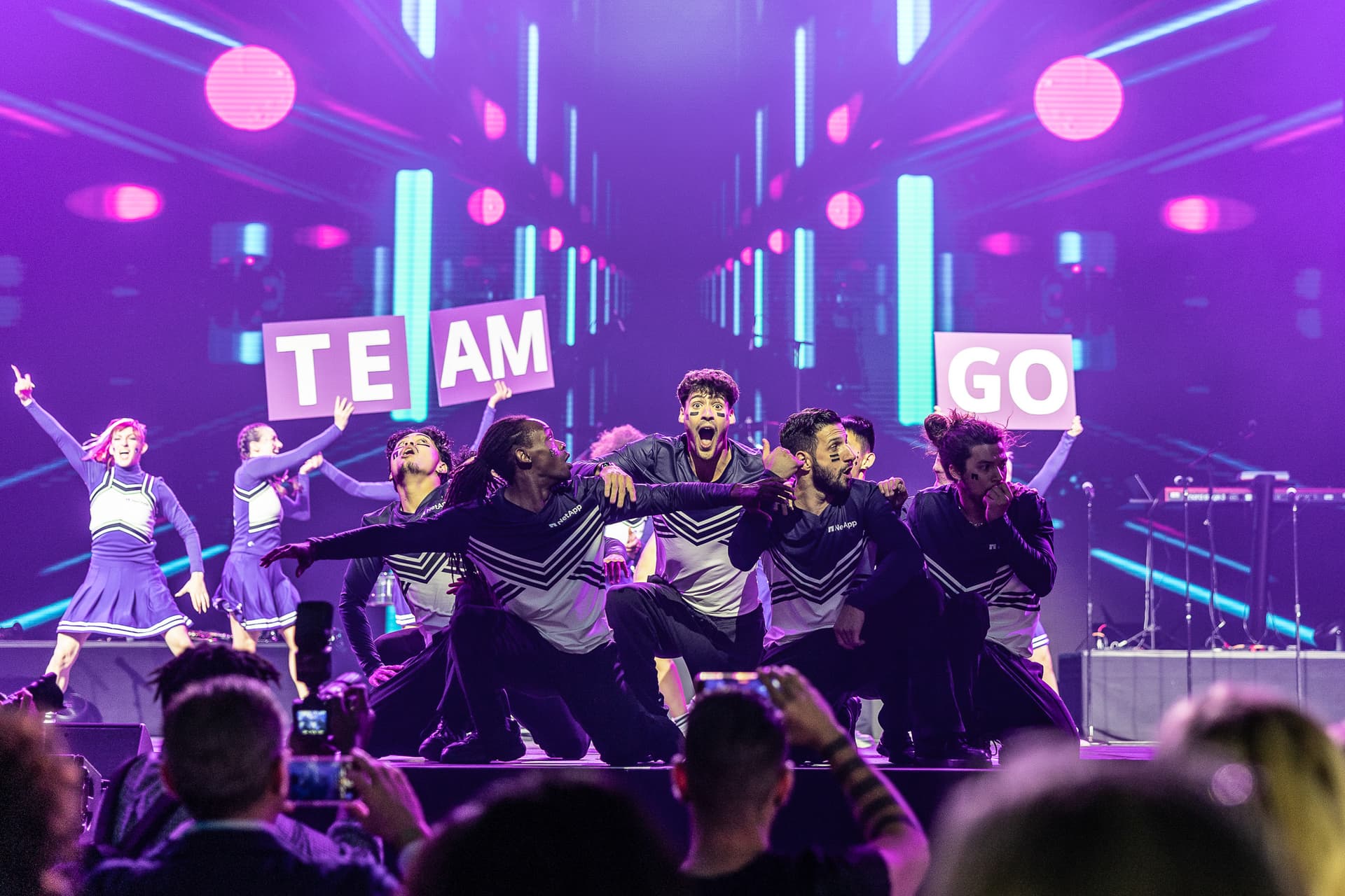 Performers in coordinated costumes dancing on stage with neon lighting design