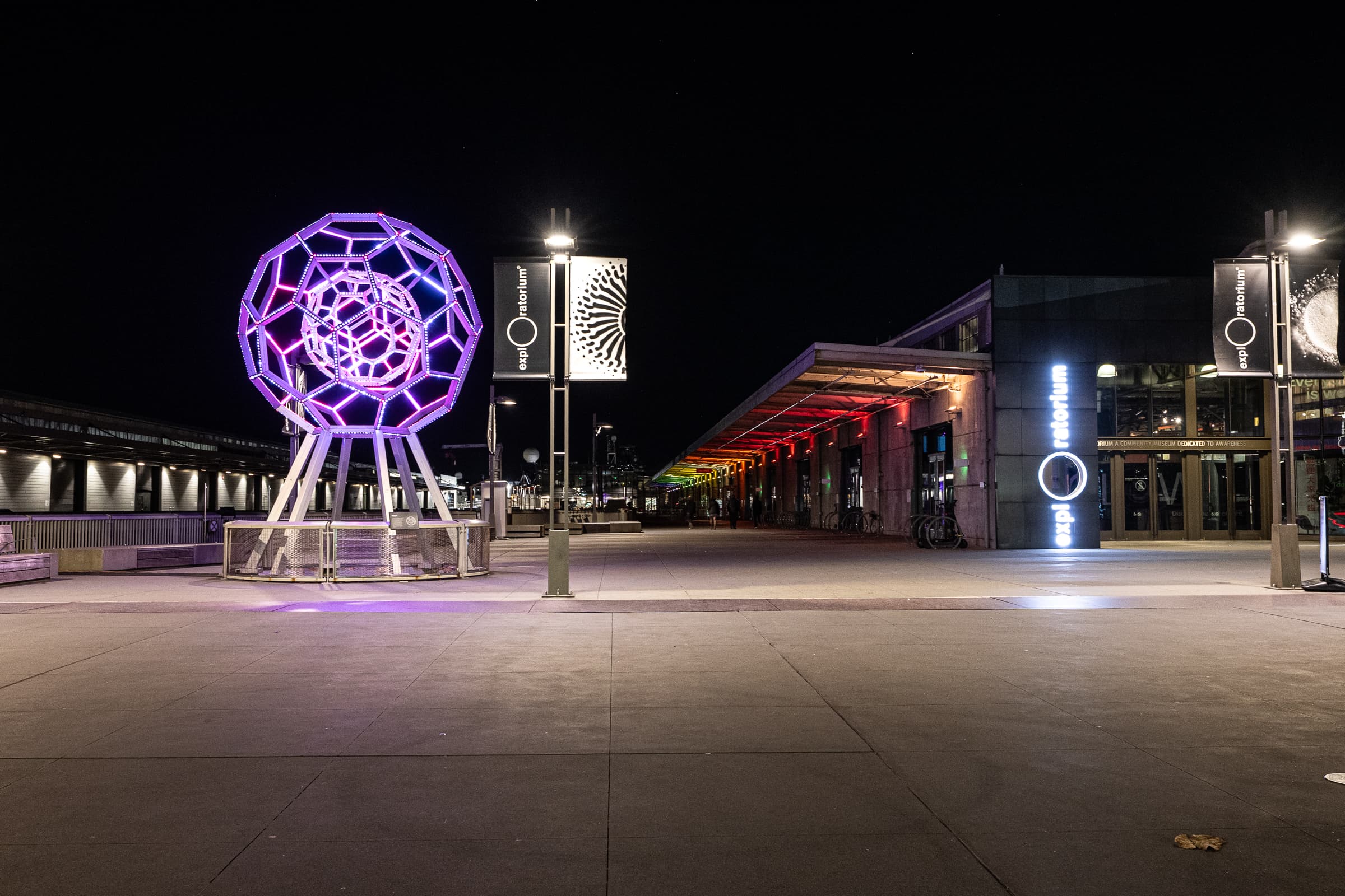 Illuminated geometric sculpture on a plaza after dark