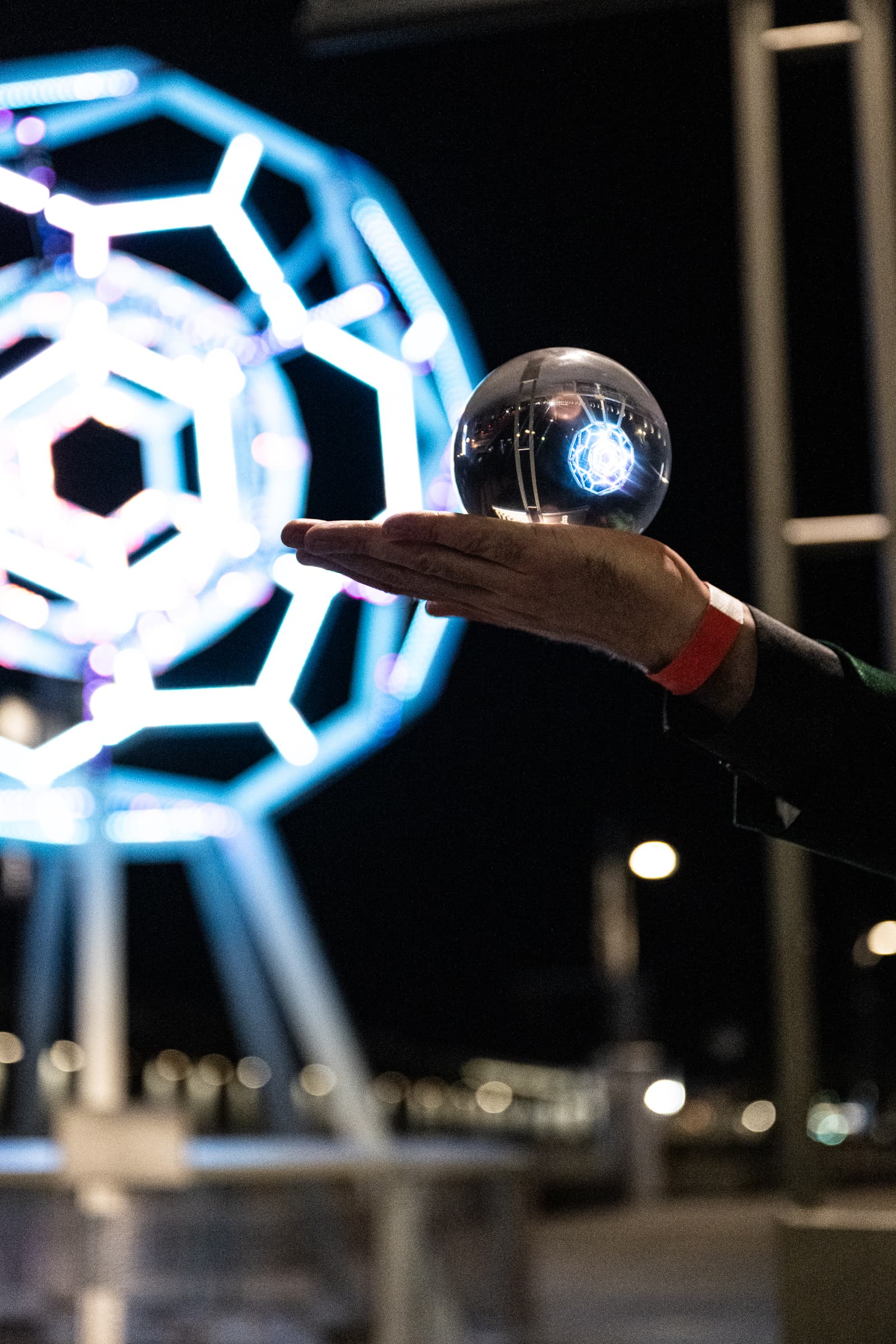 Hand balancing a glass sphere in front of an illuminated geometric installation
