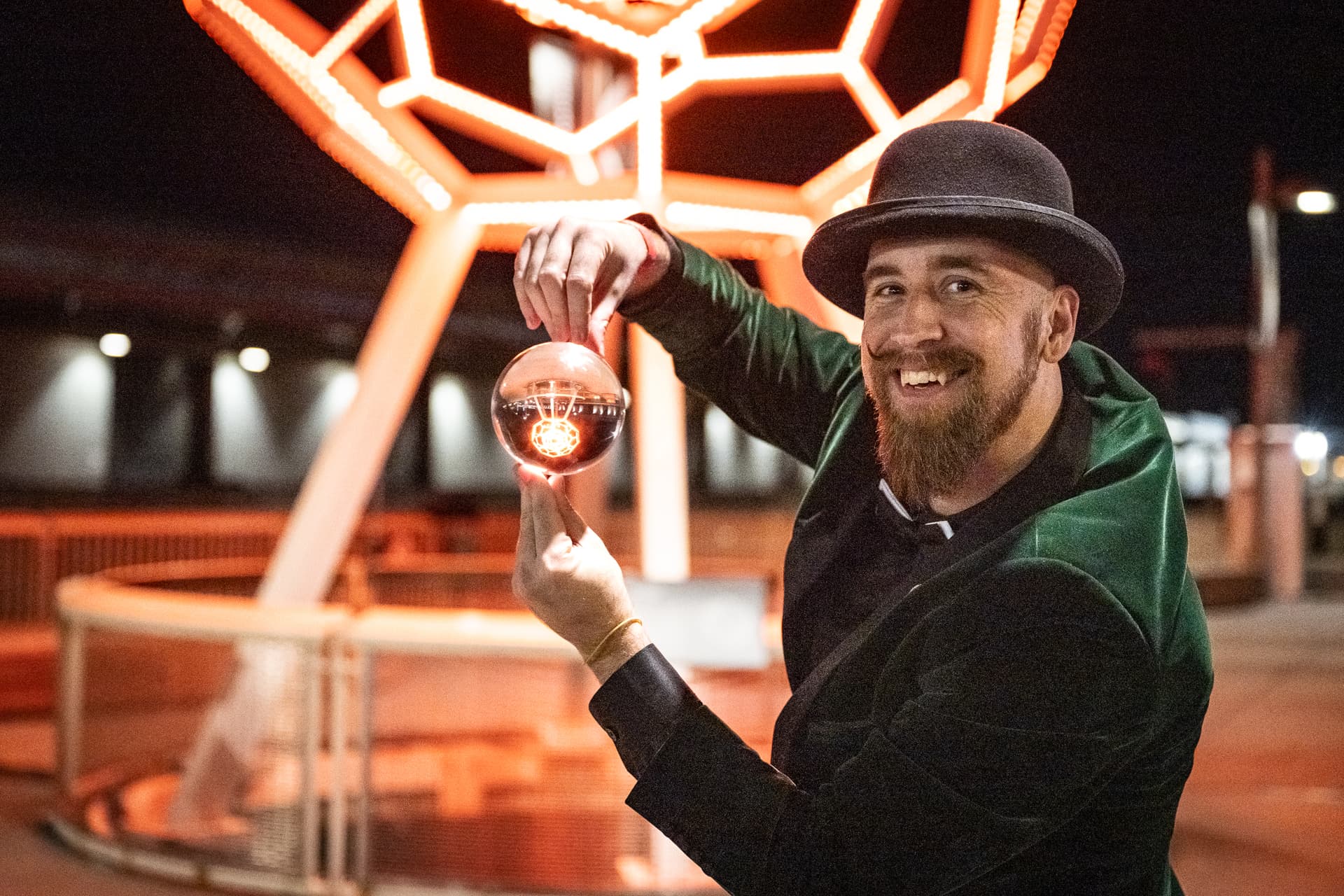 Close-up magician balancing a clear sphere beneath a geometric light sculpture