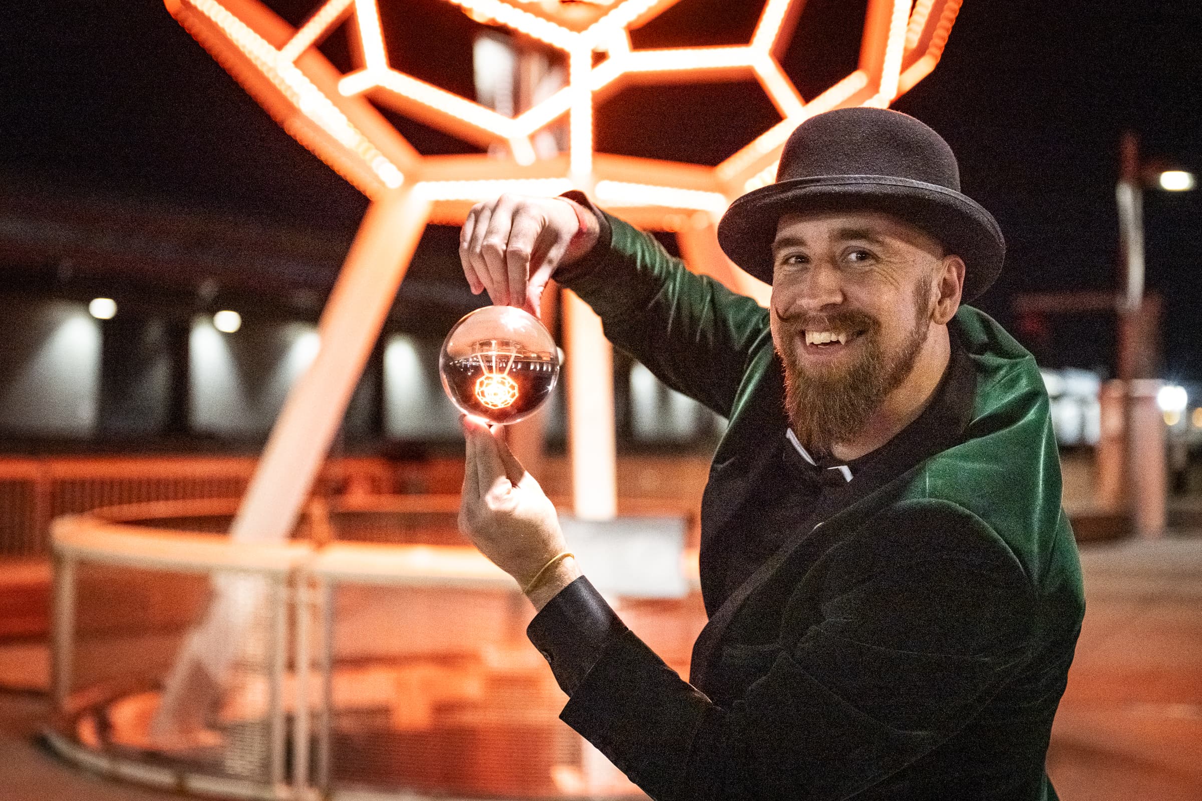 Close-up magician balancing a clear sphere beneath a geometric light sculpture