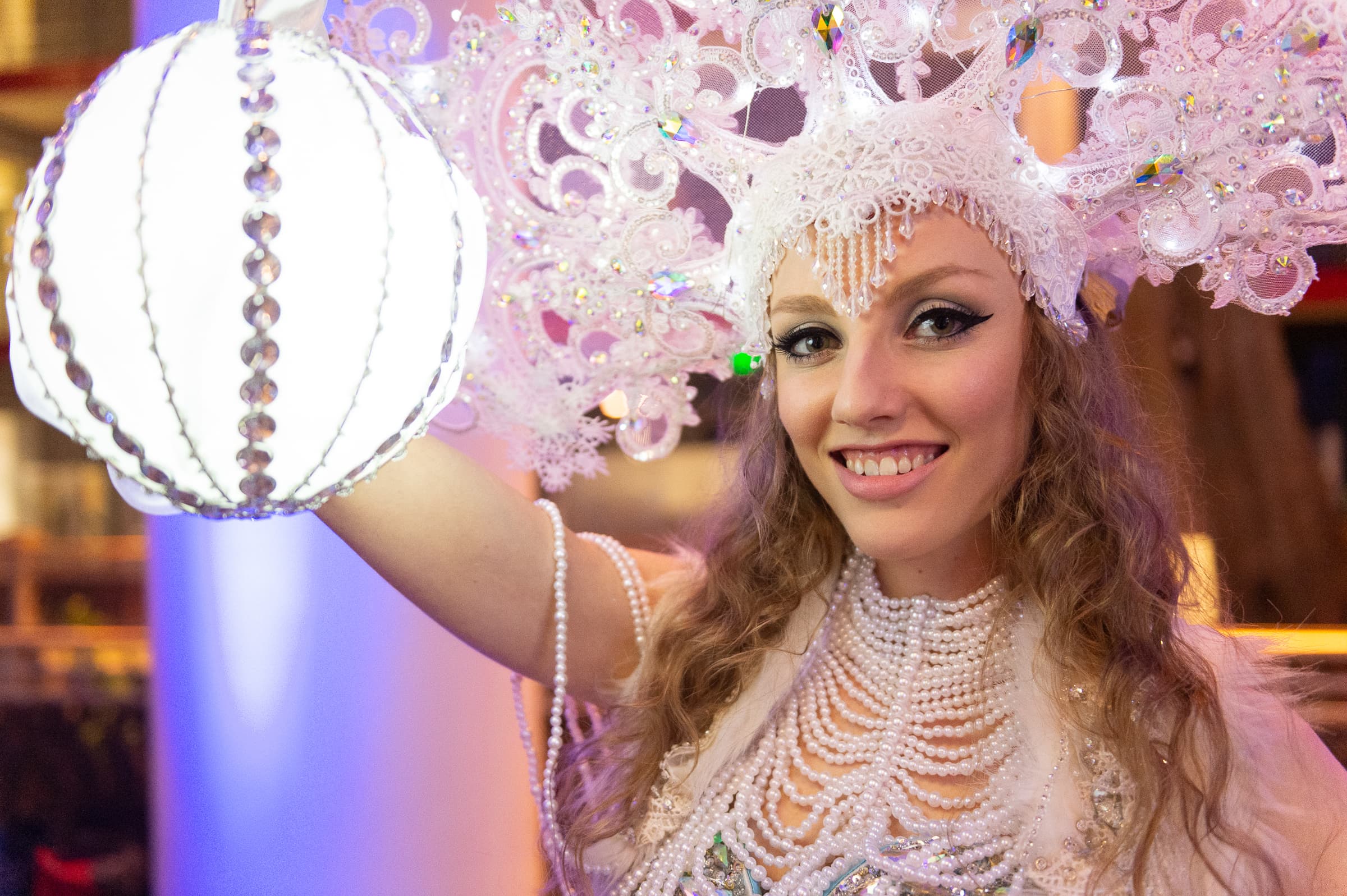 Costumed performer in an elaborate pearl headdress holding a lit orb