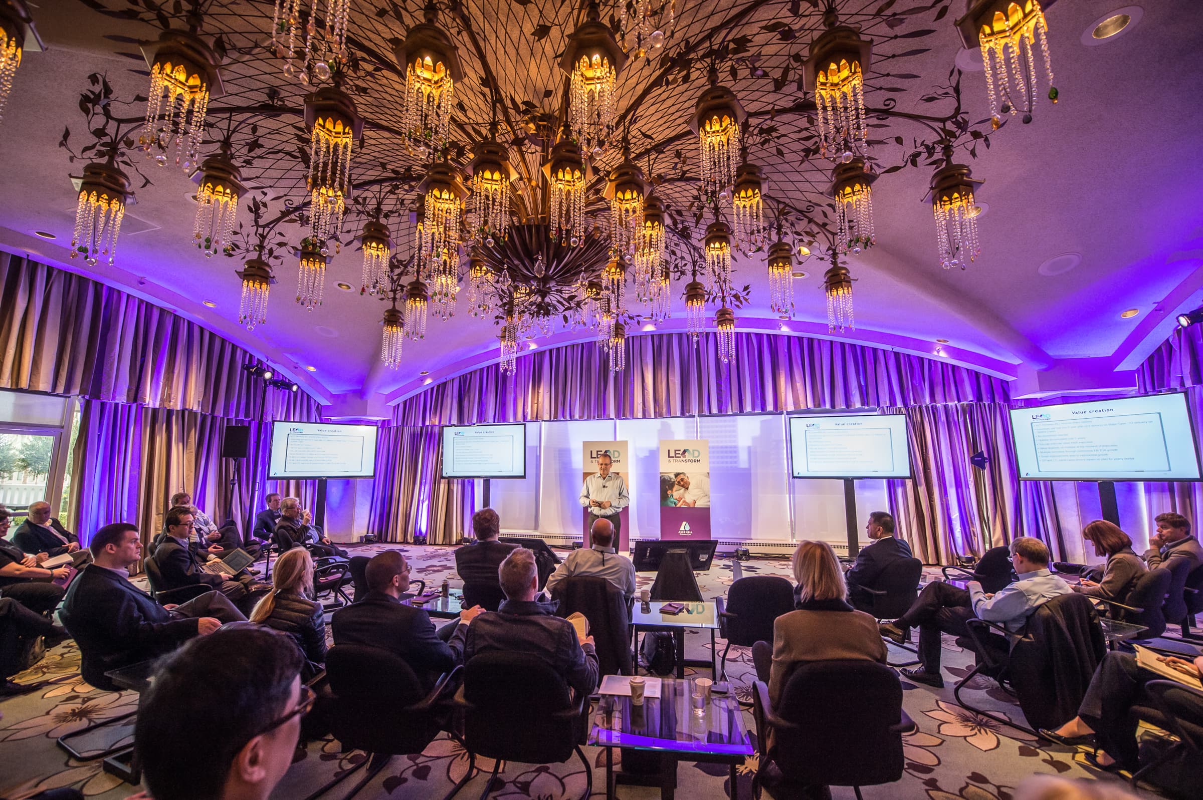 Panel session under chandeliers with an audience seated in rows