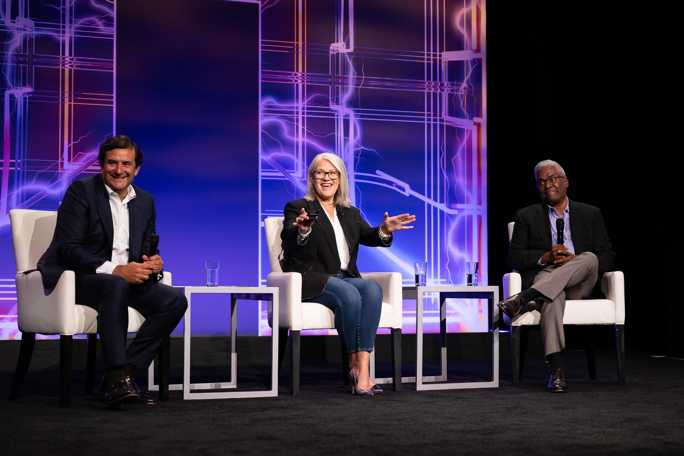 Three panellists in armchairs on a stage lit magenta and purple