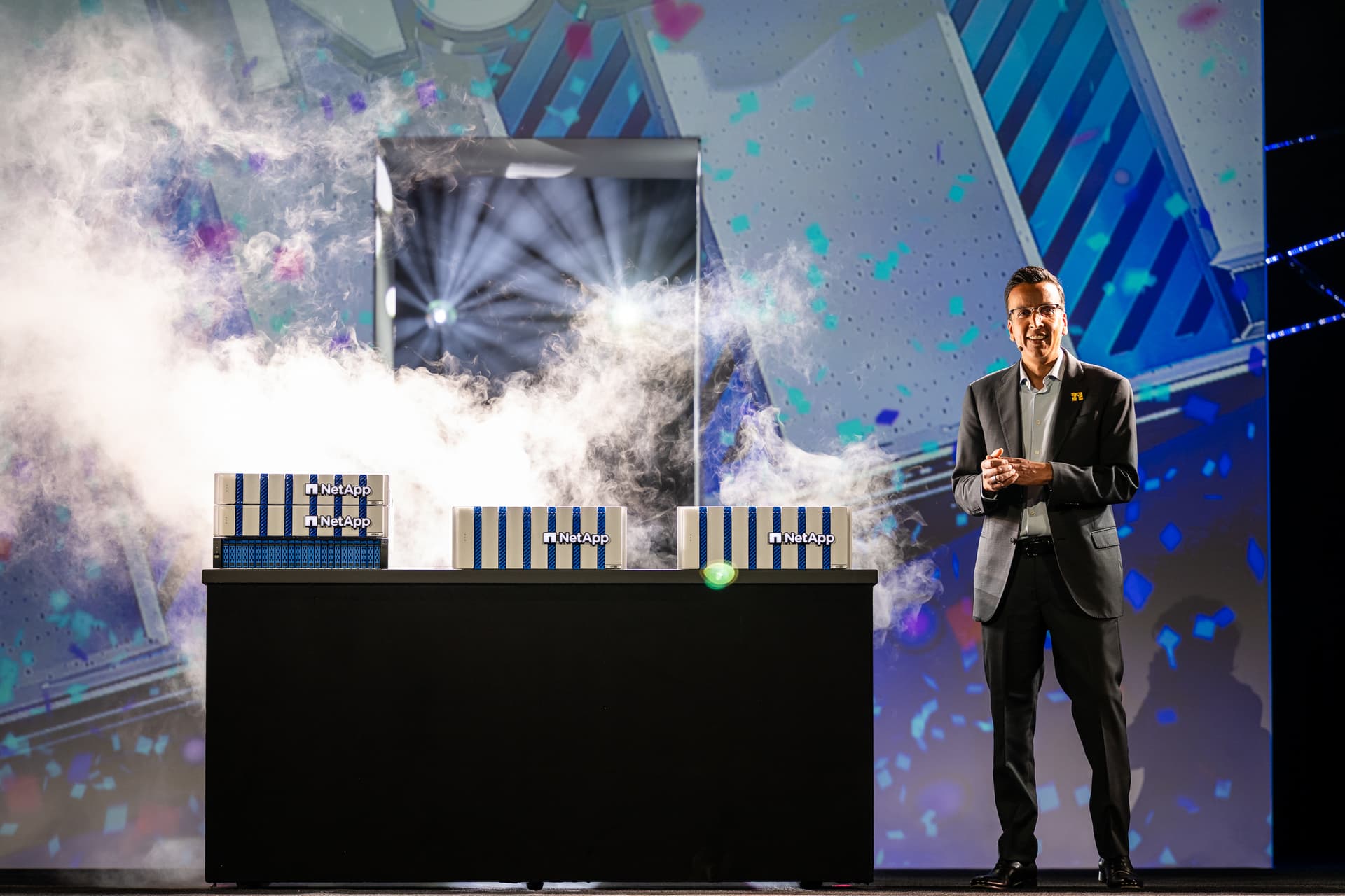 Executive presenter on stage with dramatic atmospheric effects and branded display