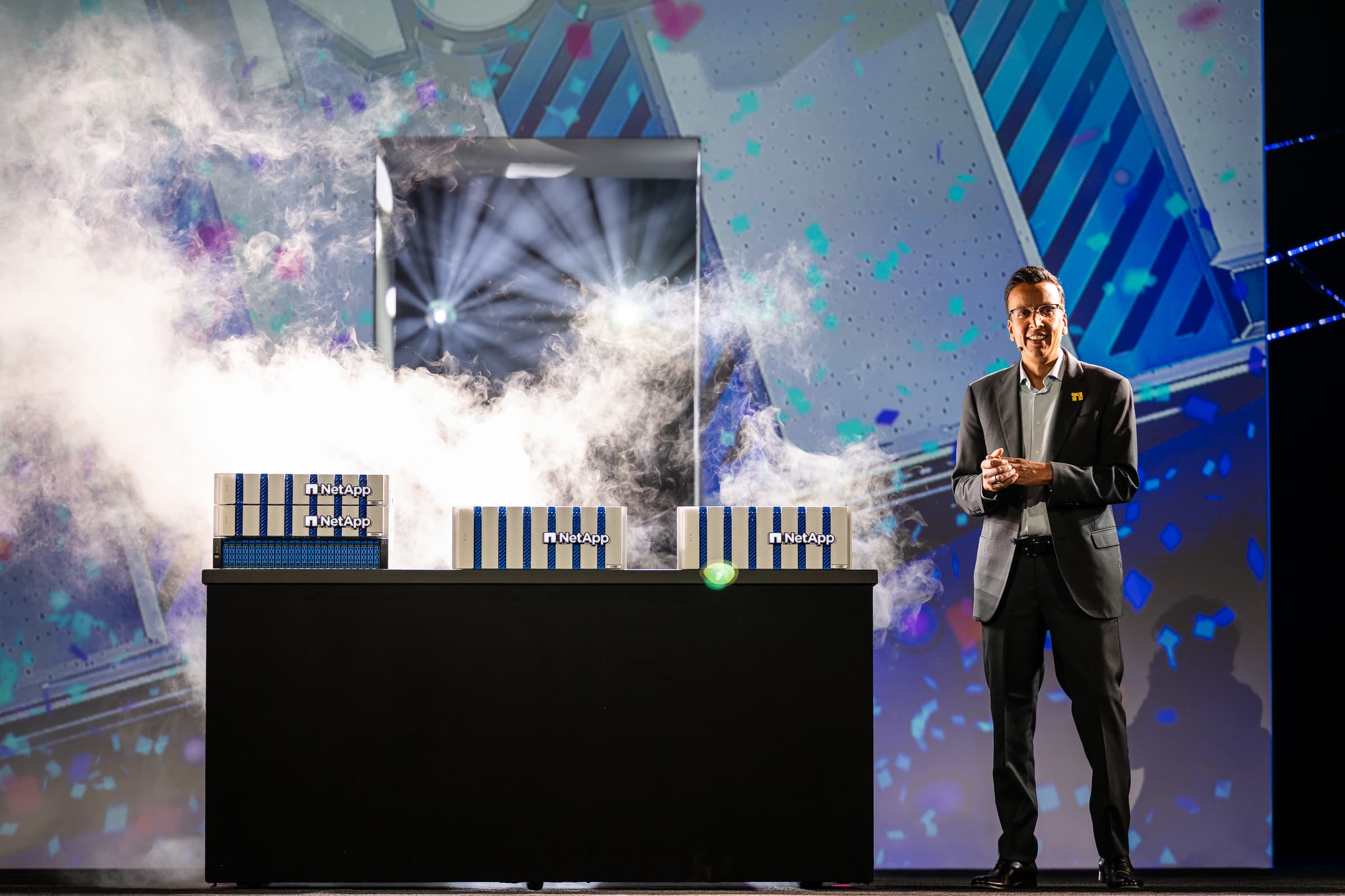Executive presenter on stage with dramatic atmospheric effects and branded display