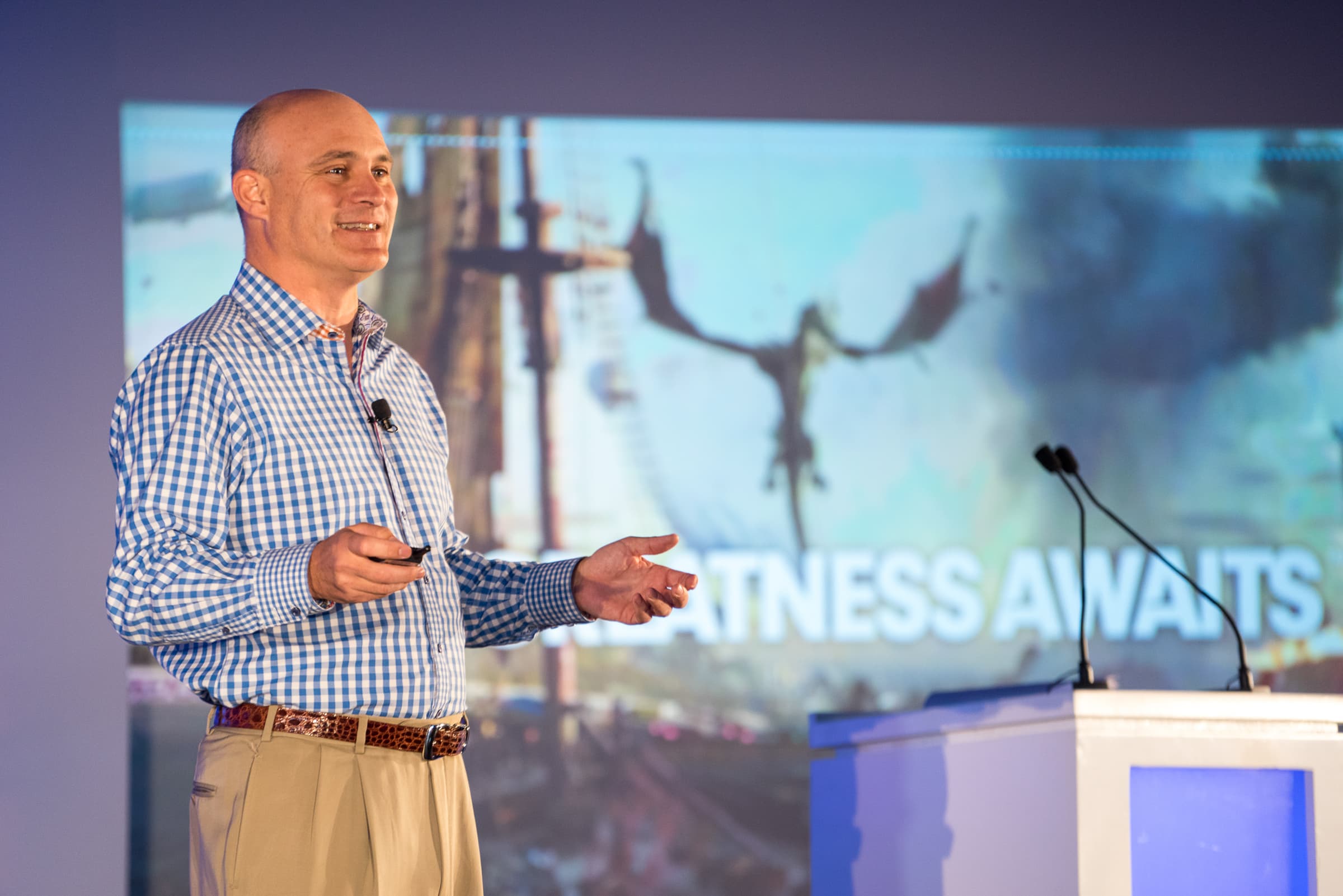 Presenter on stage gesturing toward a large screen mid-presentation