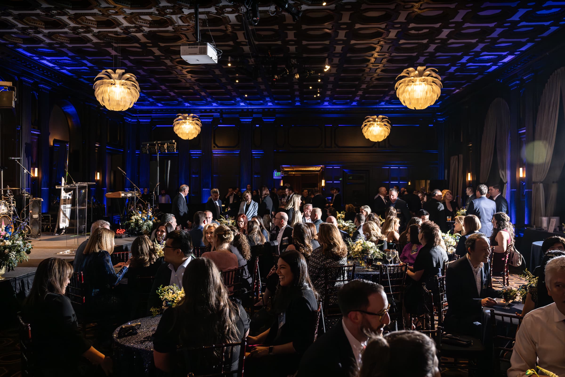 Guests seated at banquet rounds in a ballroom under blue uplighting