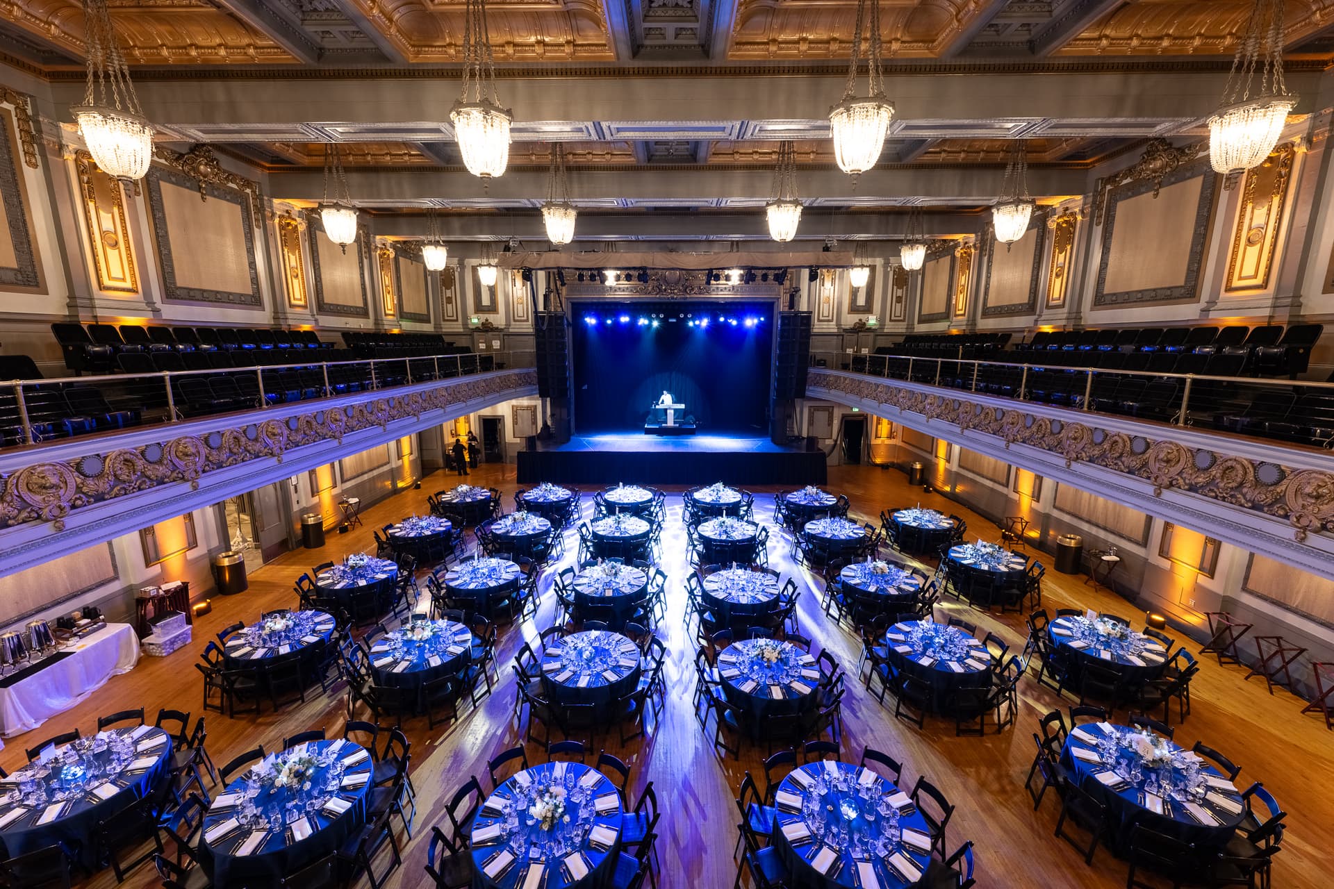 Theatre ballroom set with banquet rounds under deep blue uplighting before doors