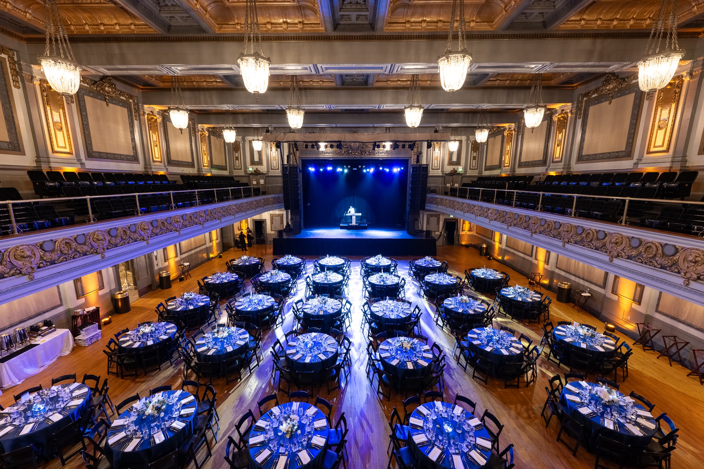 Theatre ballroom set with banquet rounds under deep blue uplighting before doors
