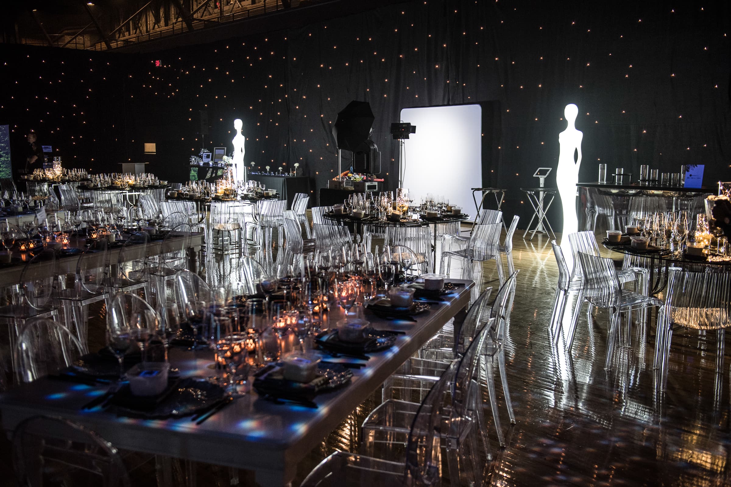 Long banquet tables laid with silver and glass beside sculptural figures