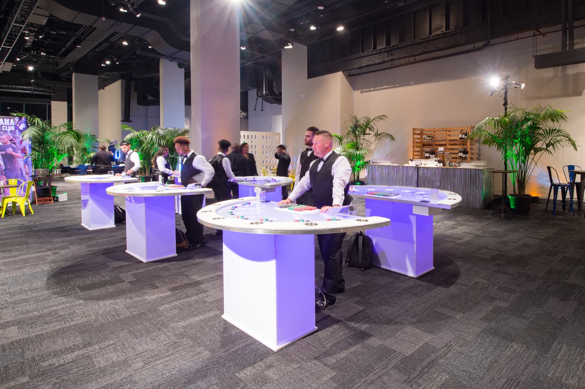 Guests at illuminated cocktail tables under purple lighting