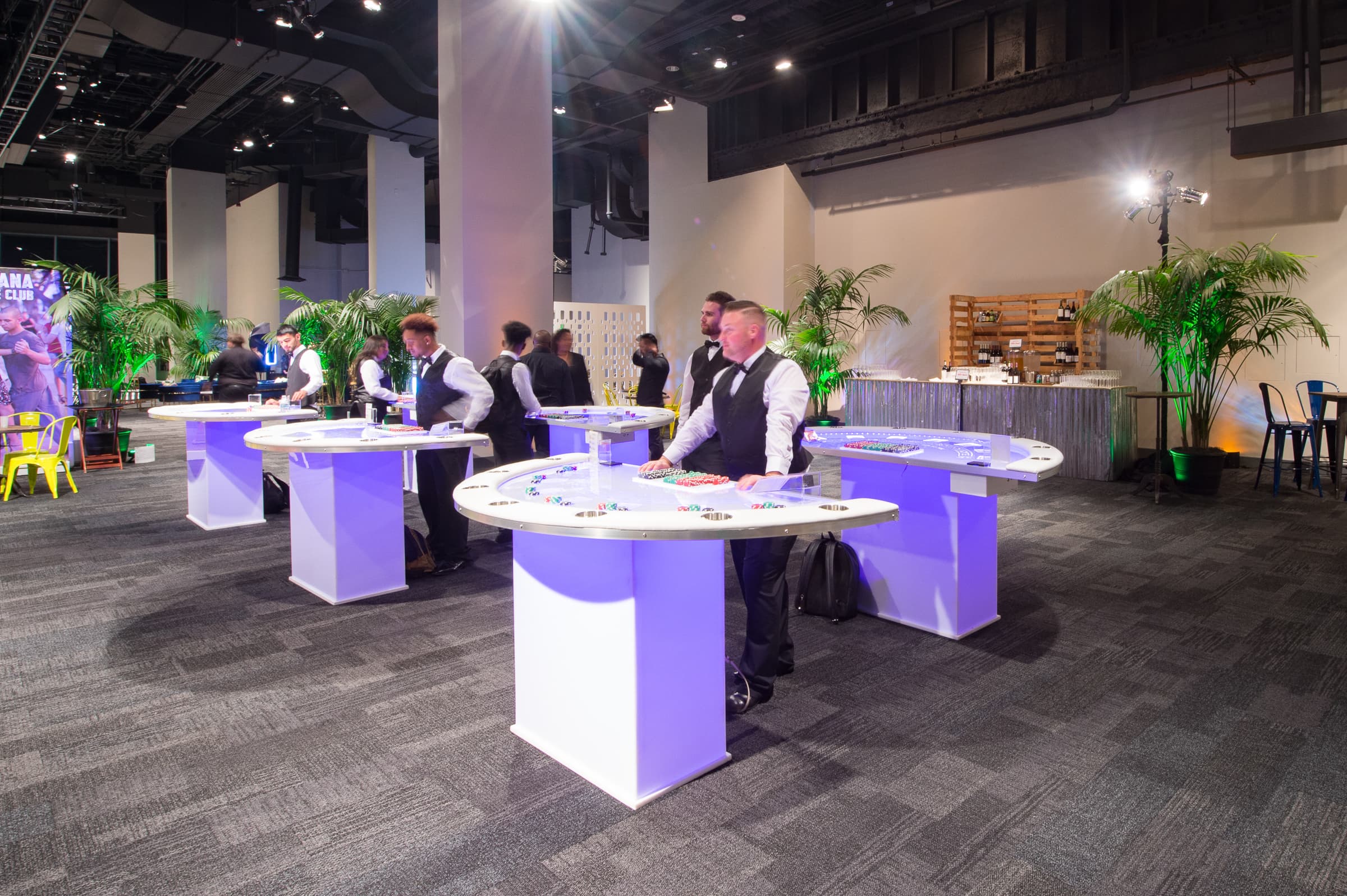 Guests at illuminated cocktail tables under purple lighting