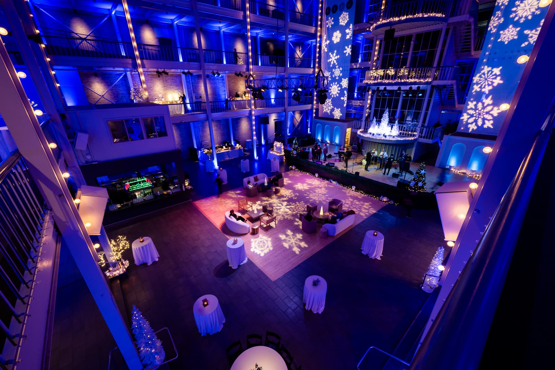 Overhead view of a holiday reception setup with blue lighting and projected snowflakes in the San Francisco Design Center atrium