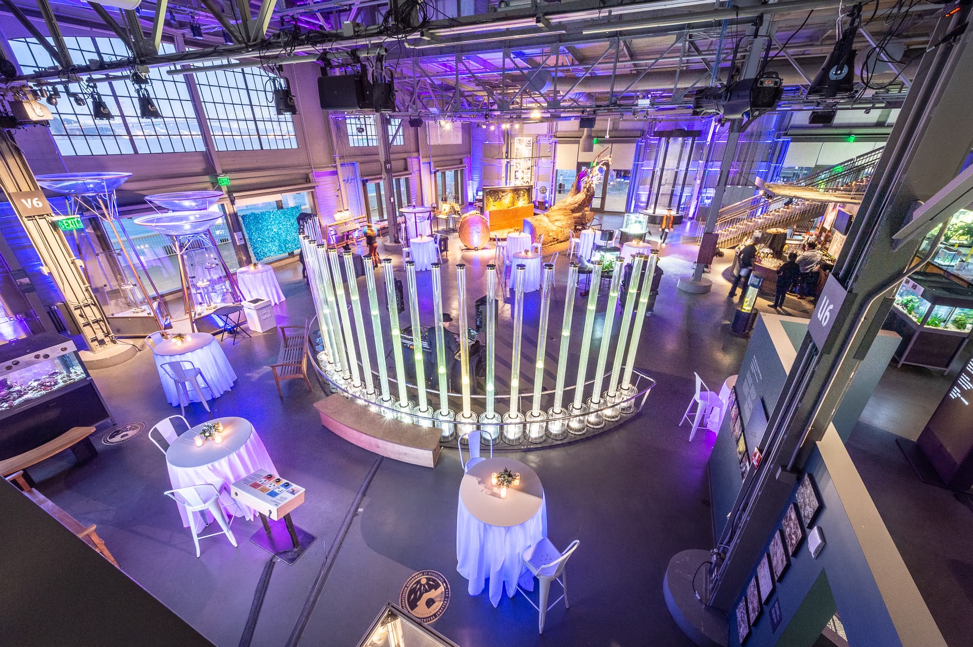 Overhead view of a holiday reception setup among Exploratorium exhibits with purple lighting and cocktail tables