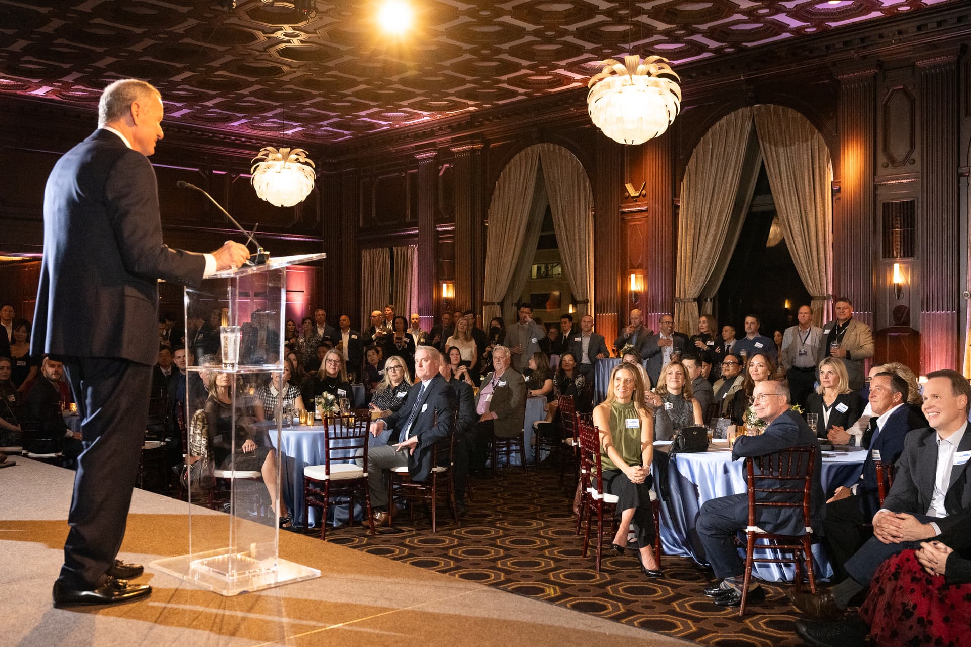 Host giving remarks from a lectern to a full ballroom