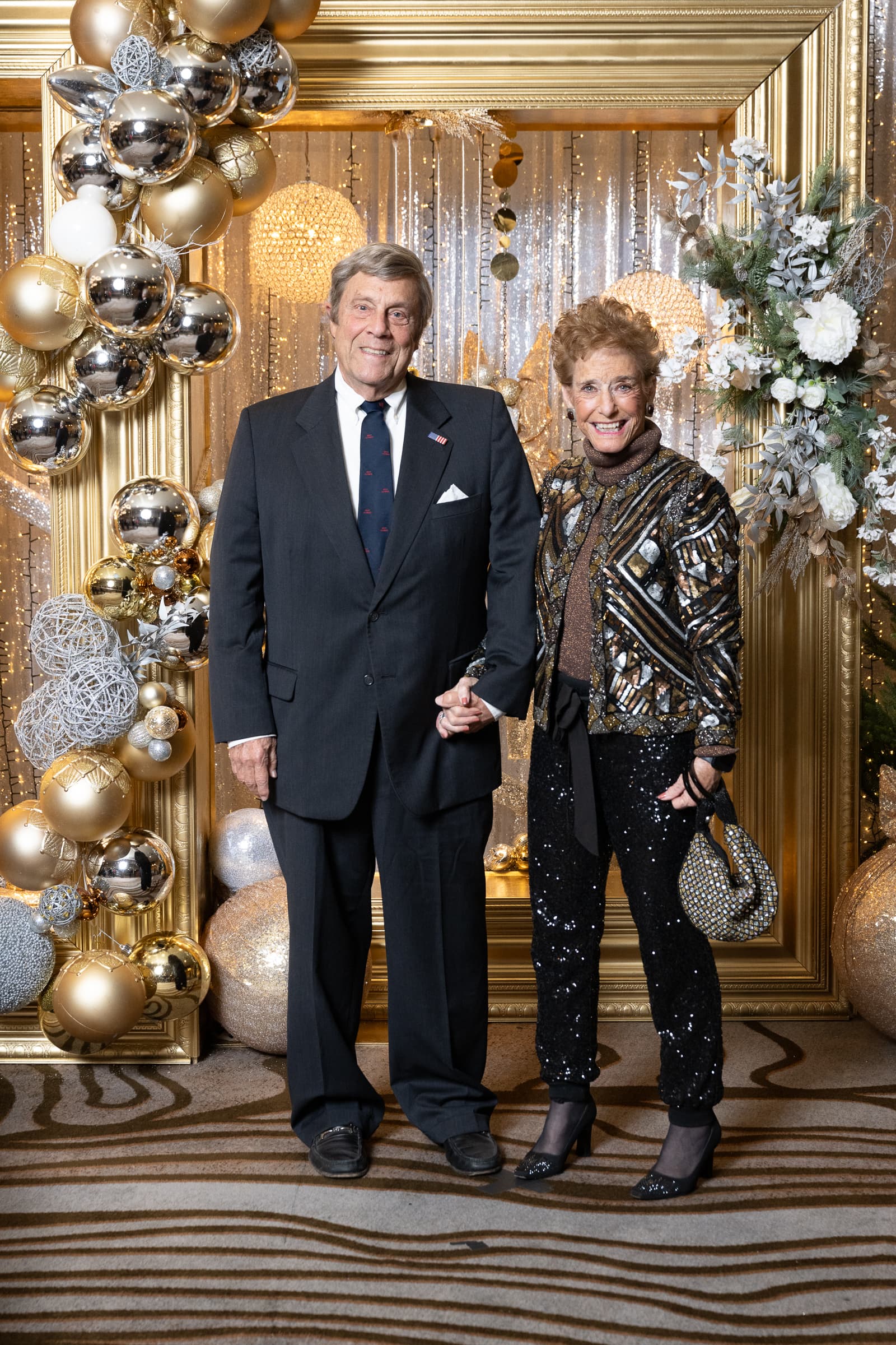 Two guests photographed against a silver and gold ornament backdrop