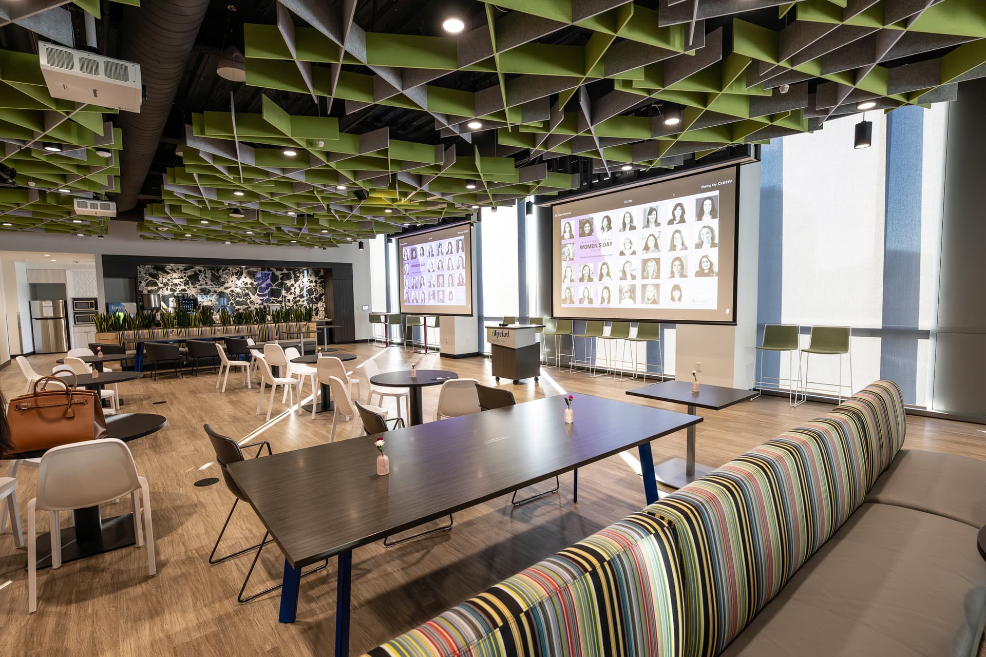 Tables and chairs facing presentation screens beneath a green geometric ceiling at Myriad Genetics