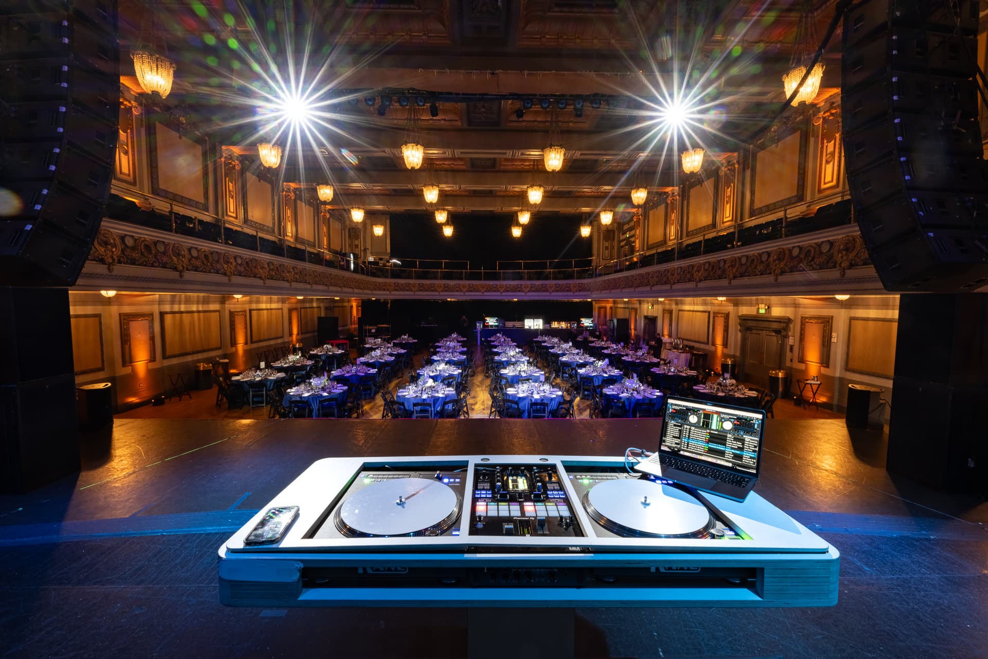 DJ turntables and laptop on stage overlooking the Regency Ballroom dinner setup and balconies