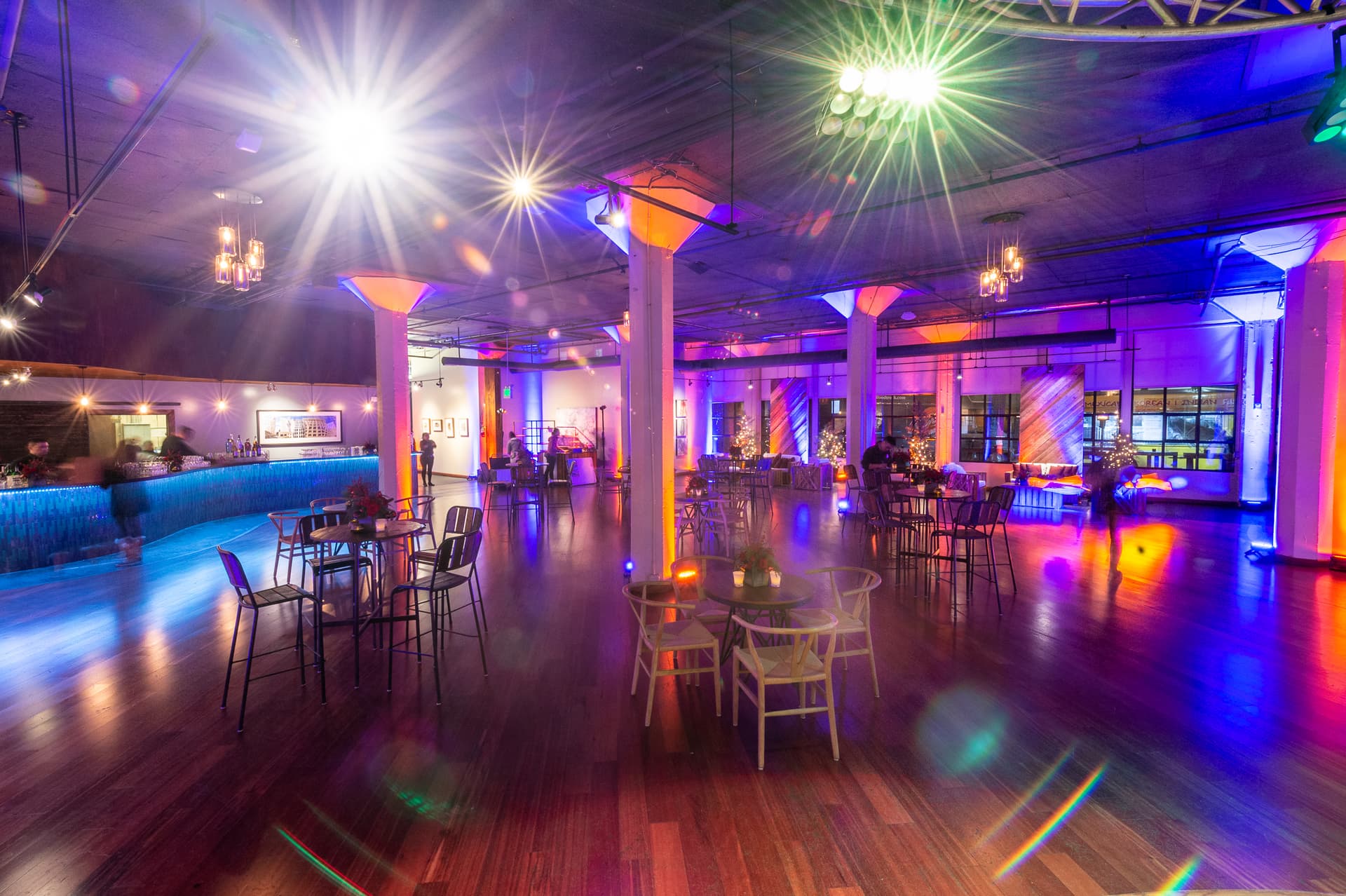 Colorful stage lighting across the wooden floor, bar, and cocktail tables at Terra Gallery