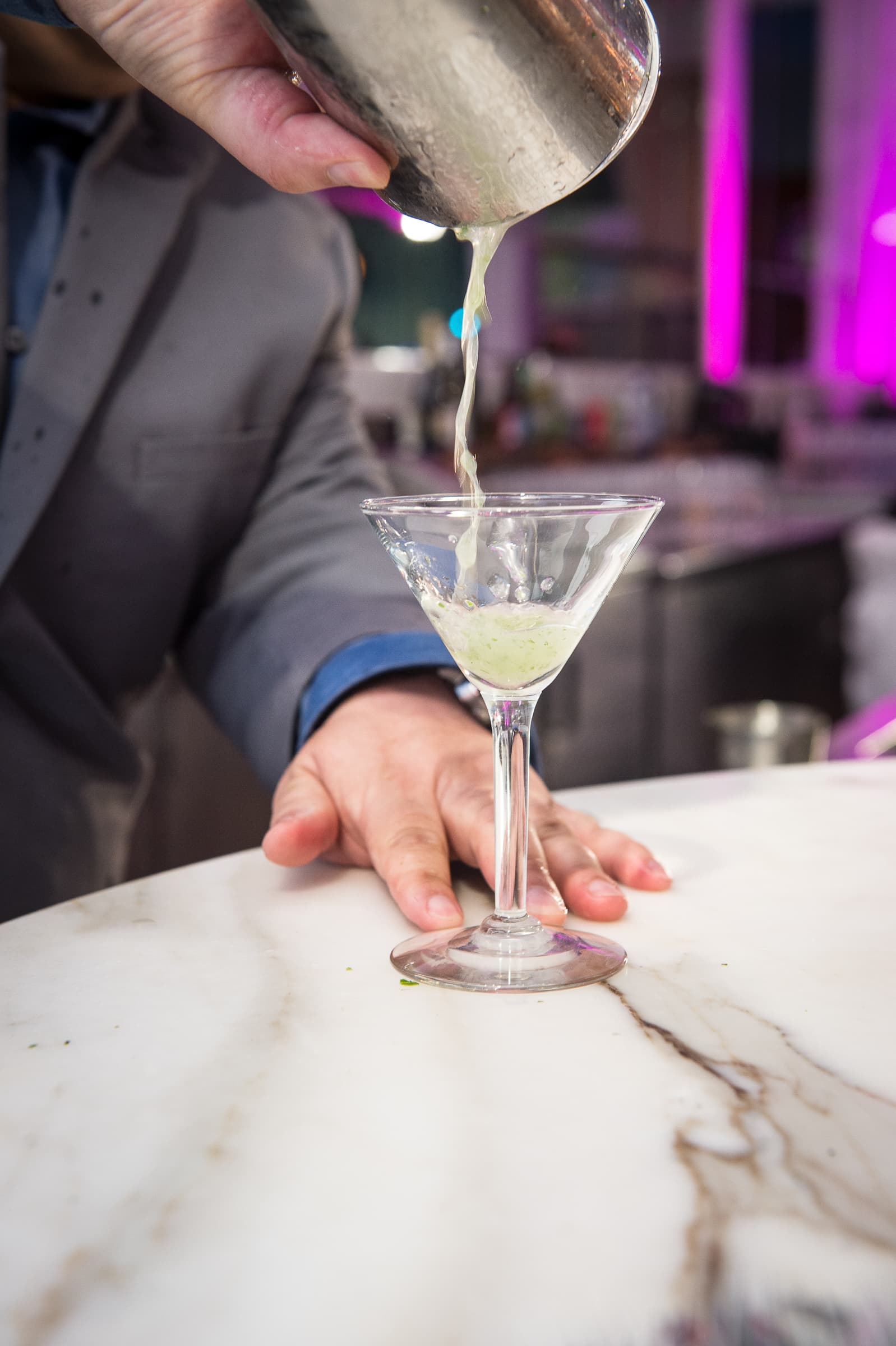 Bartender straining a martini at a marble bar