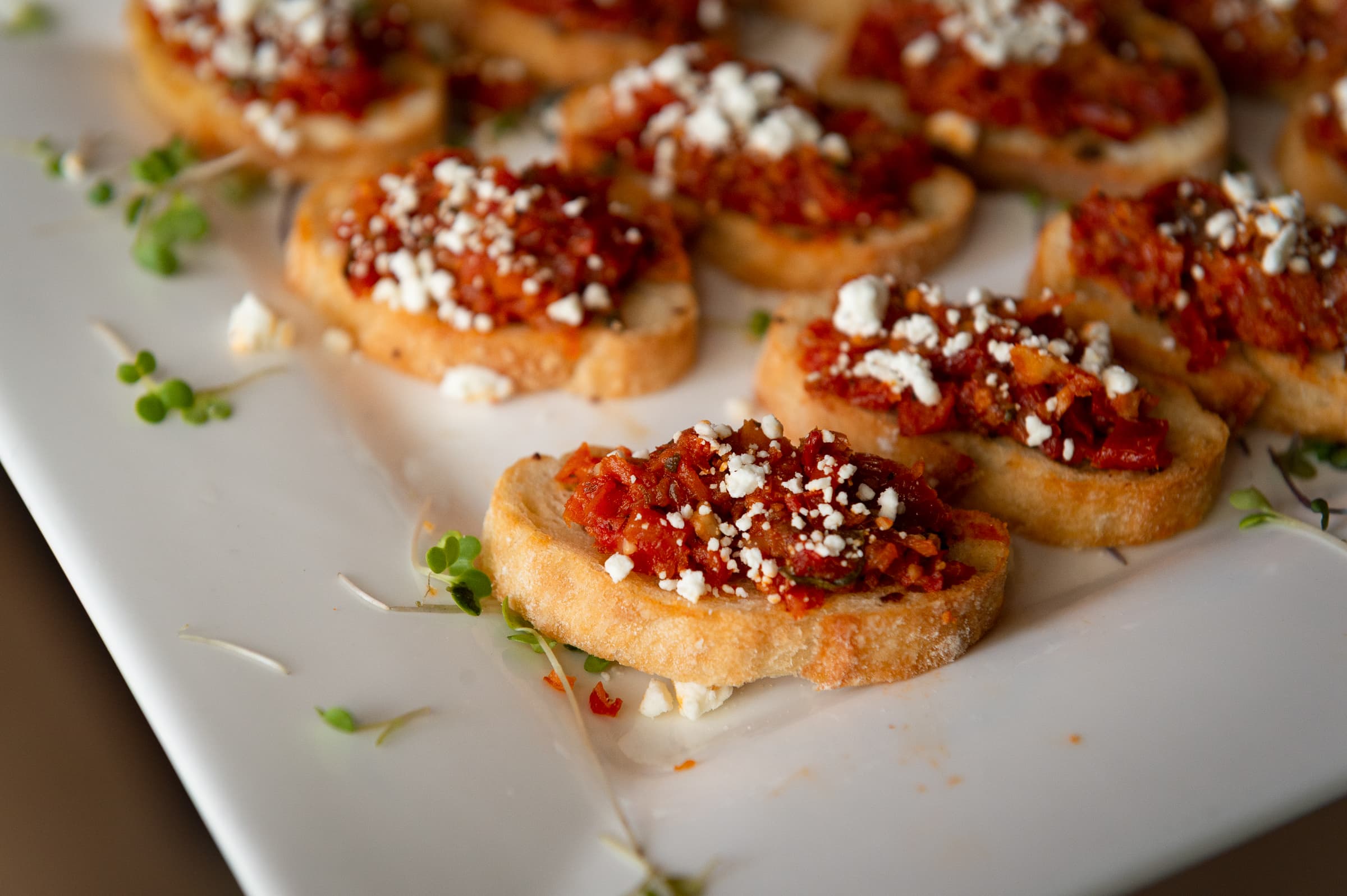 Bruschetta canapes plated in a row with fresh herb garnish