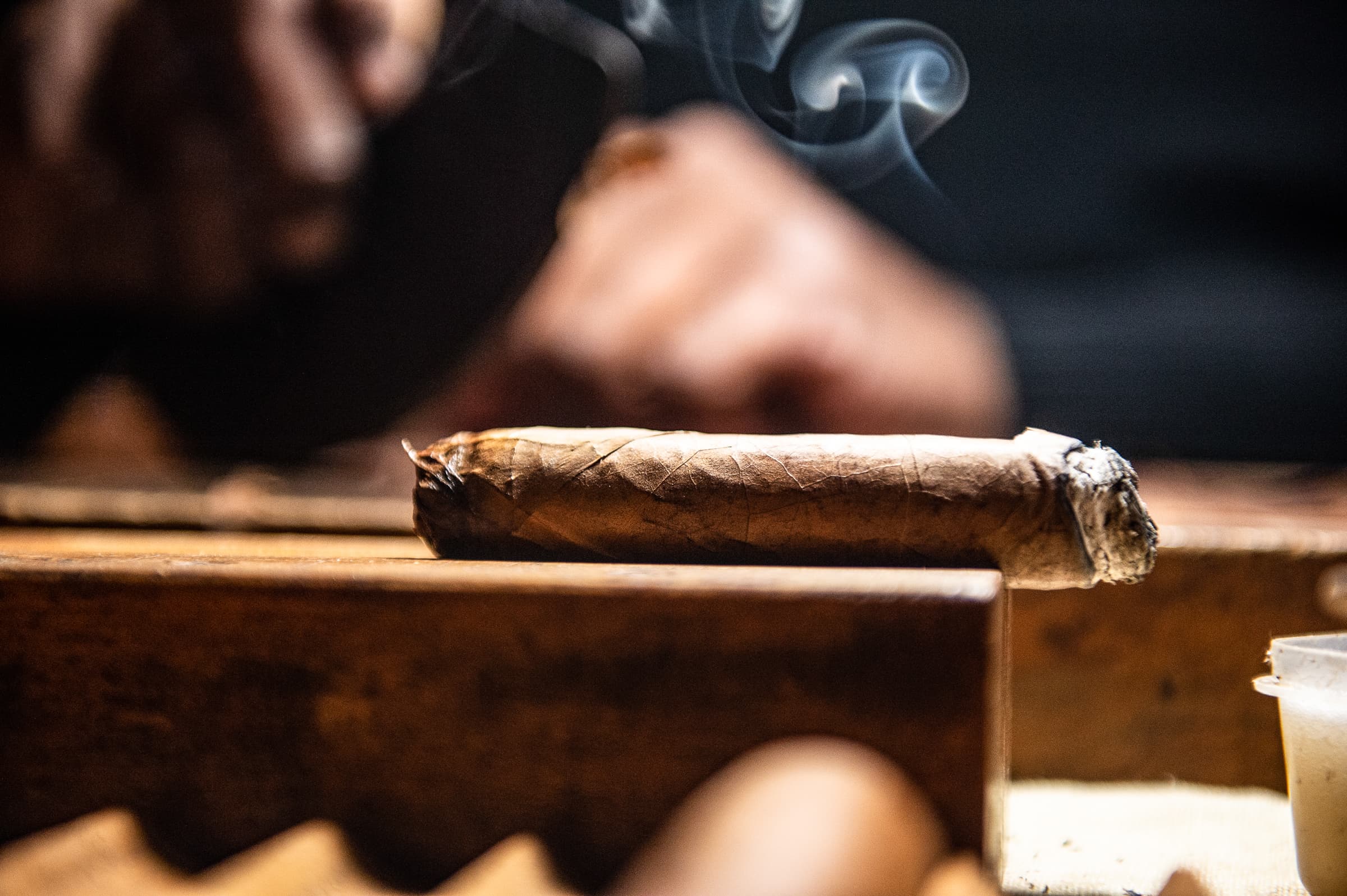 Lit cigar resting on wooden surface with wisps of smoke curling upward at upscale event lounge