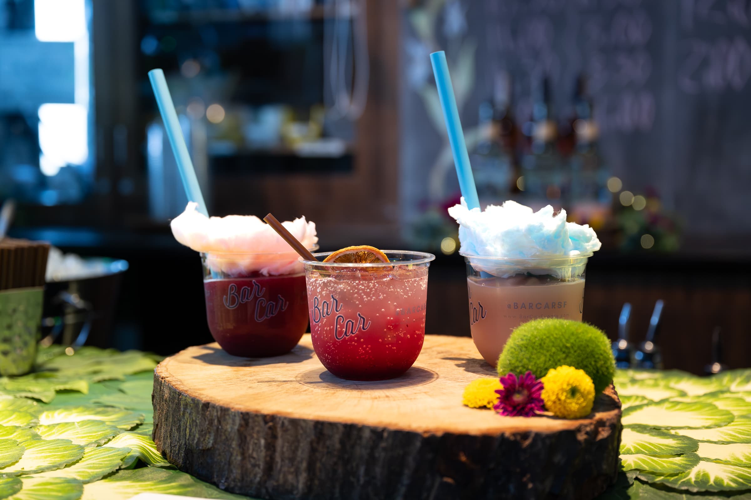 Three garnished craft cocktails arranged on a live-edge wood slab