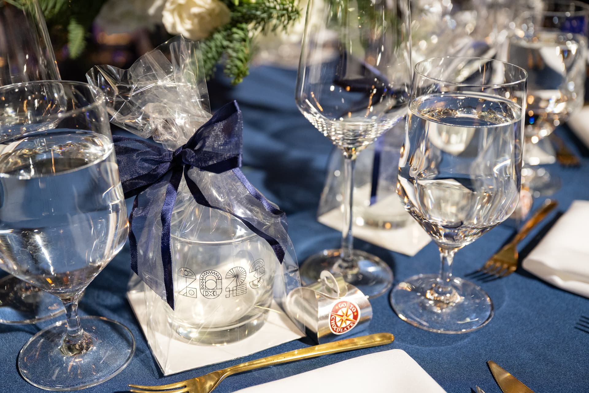 Place setting detail with navy ribbon, glassware and a wrapped favour