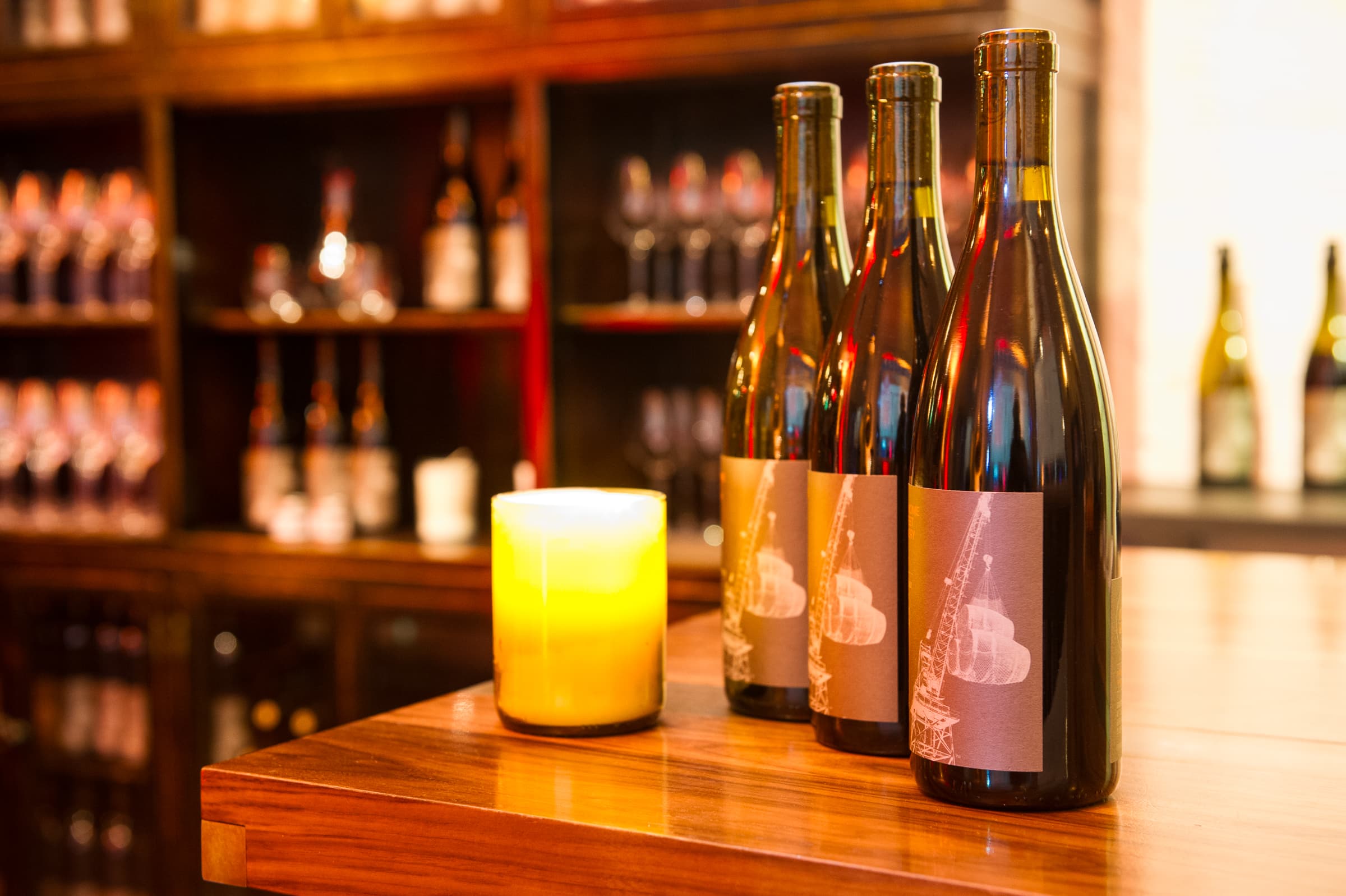 Wine bottles lined along a back bar beside a lit pillar candle