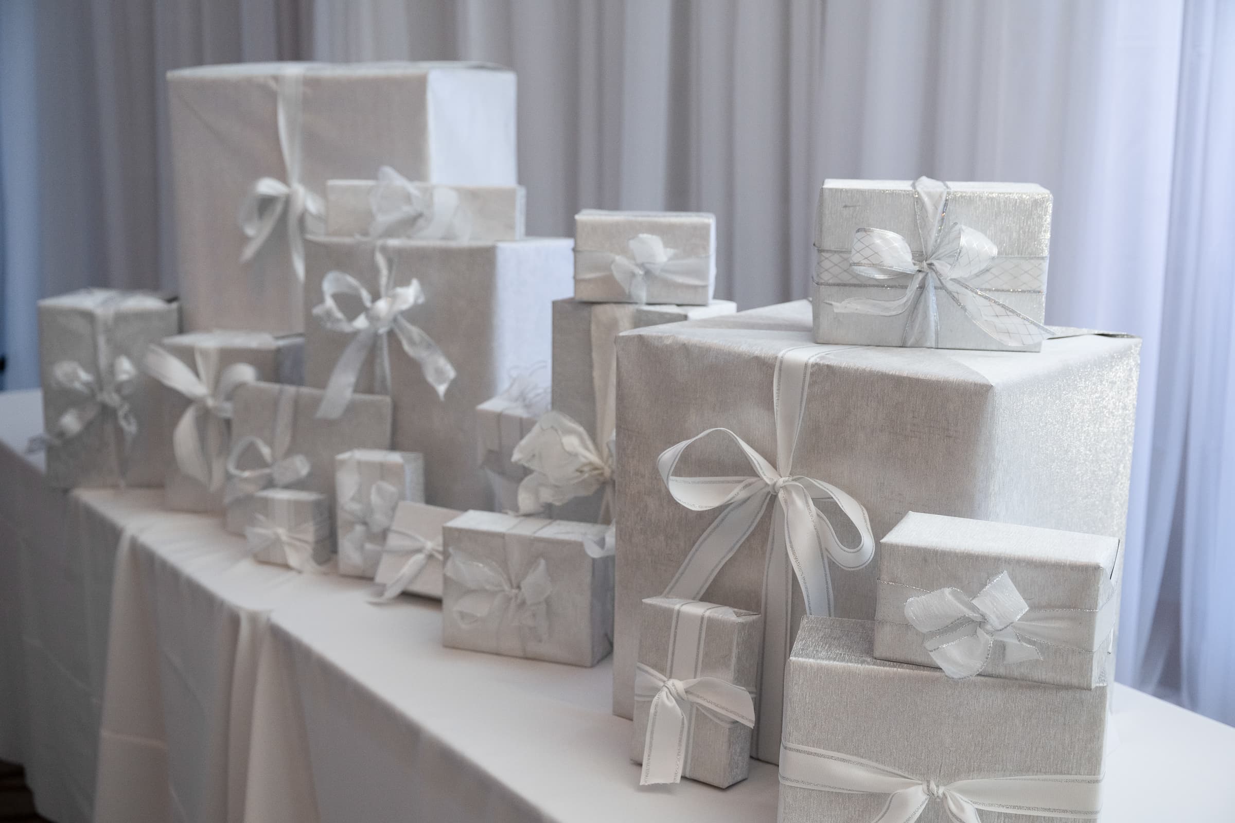 Stack of white wrapped gifts with silver ribbon on a draped table