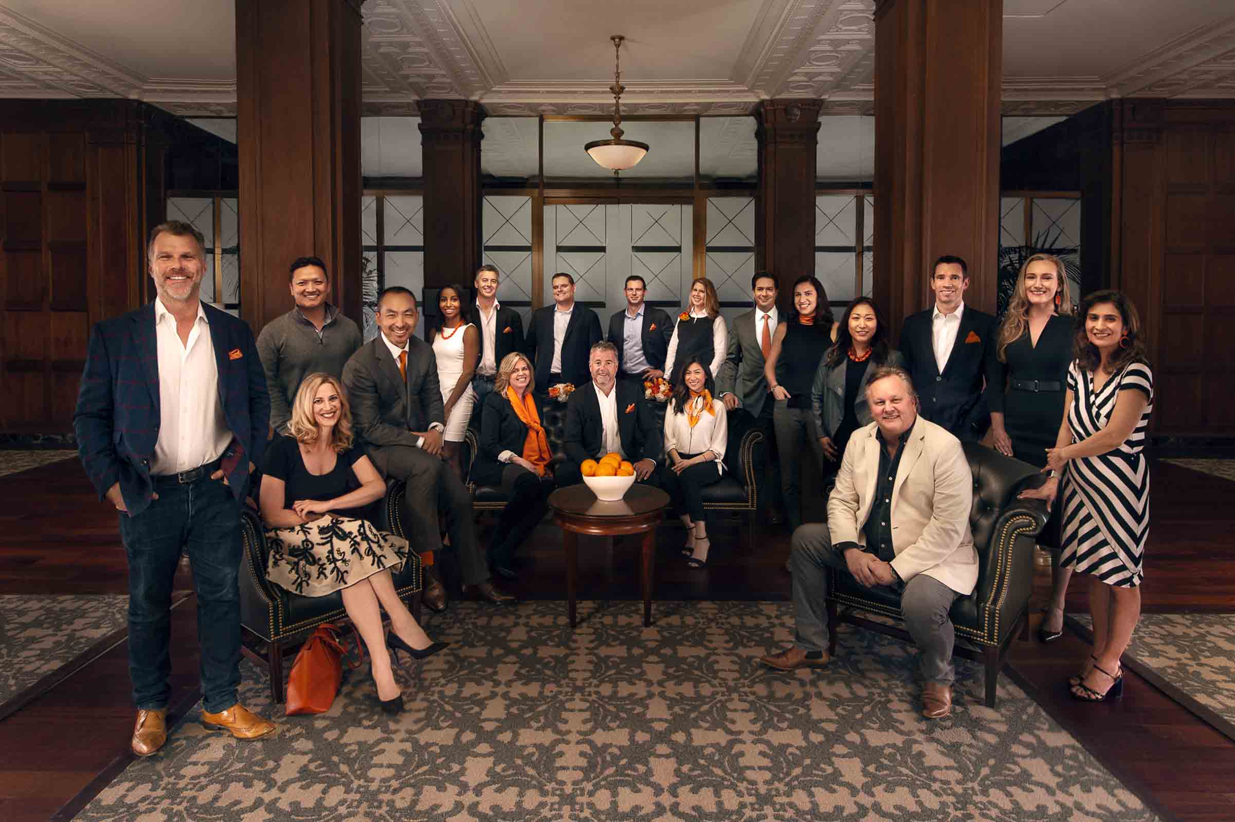 Professional corporate team portrait with coordinated orange accents in elegant wood-paneled lobby