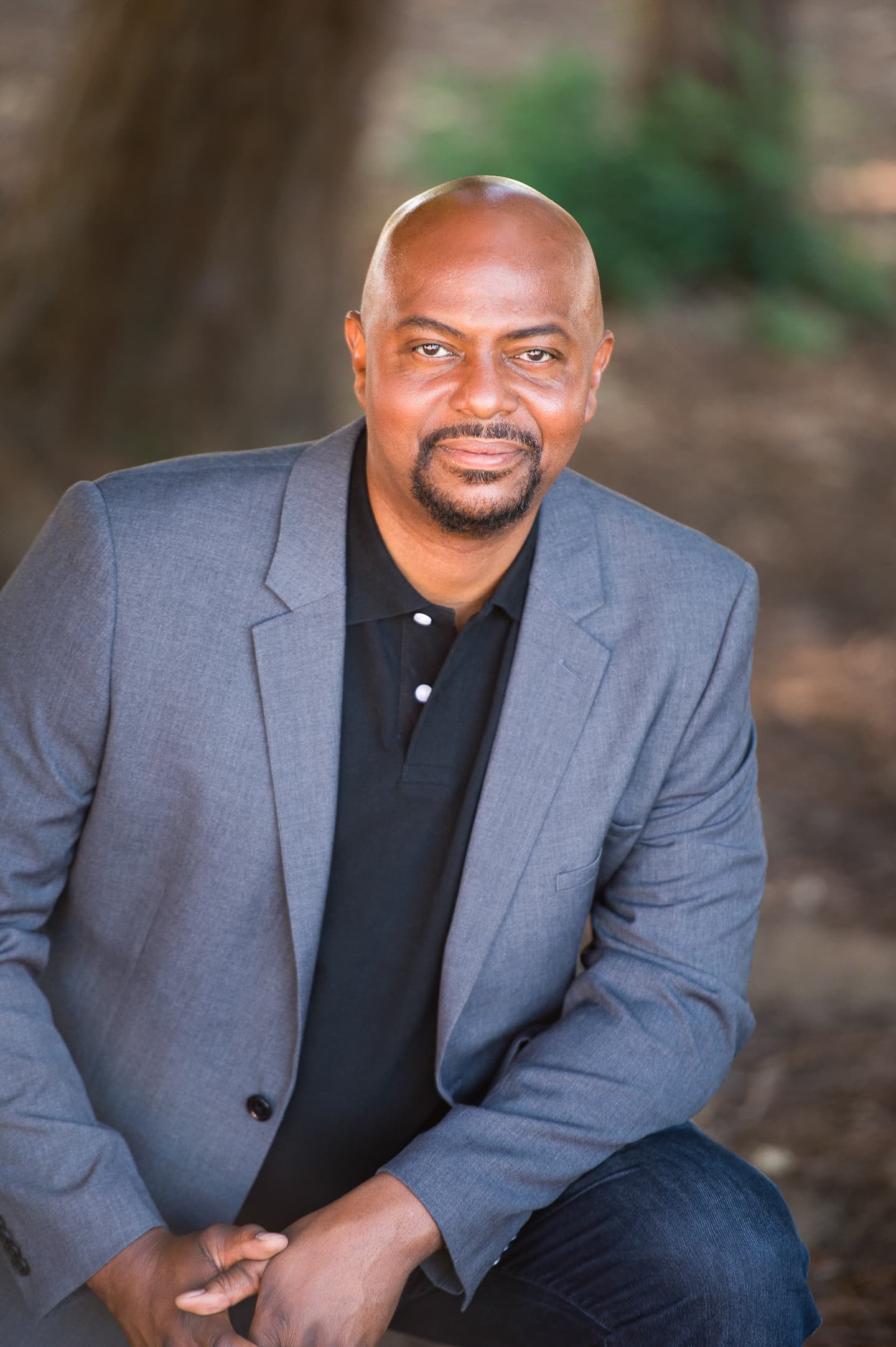 Professional headshot of executive in gray blazer with outdoor setting