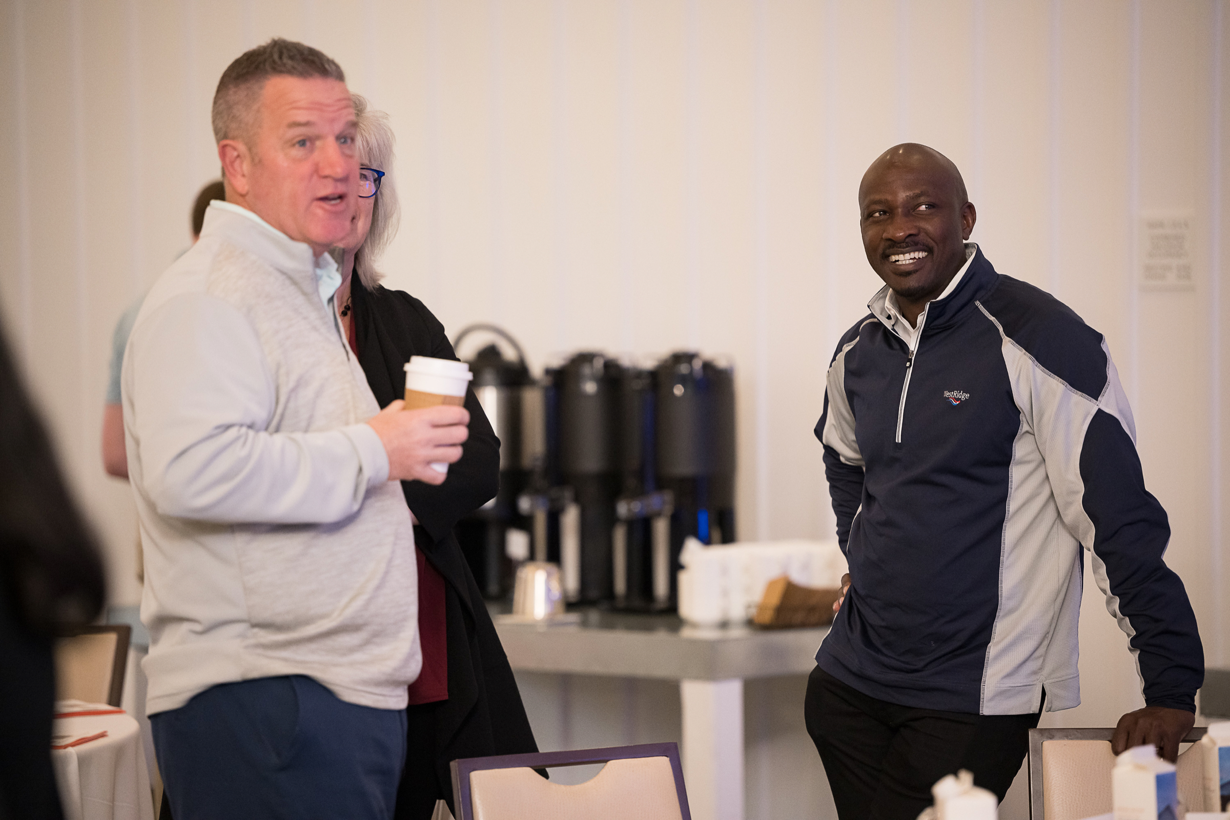 Two guests talking beside the coffee urns at a hosted morning session