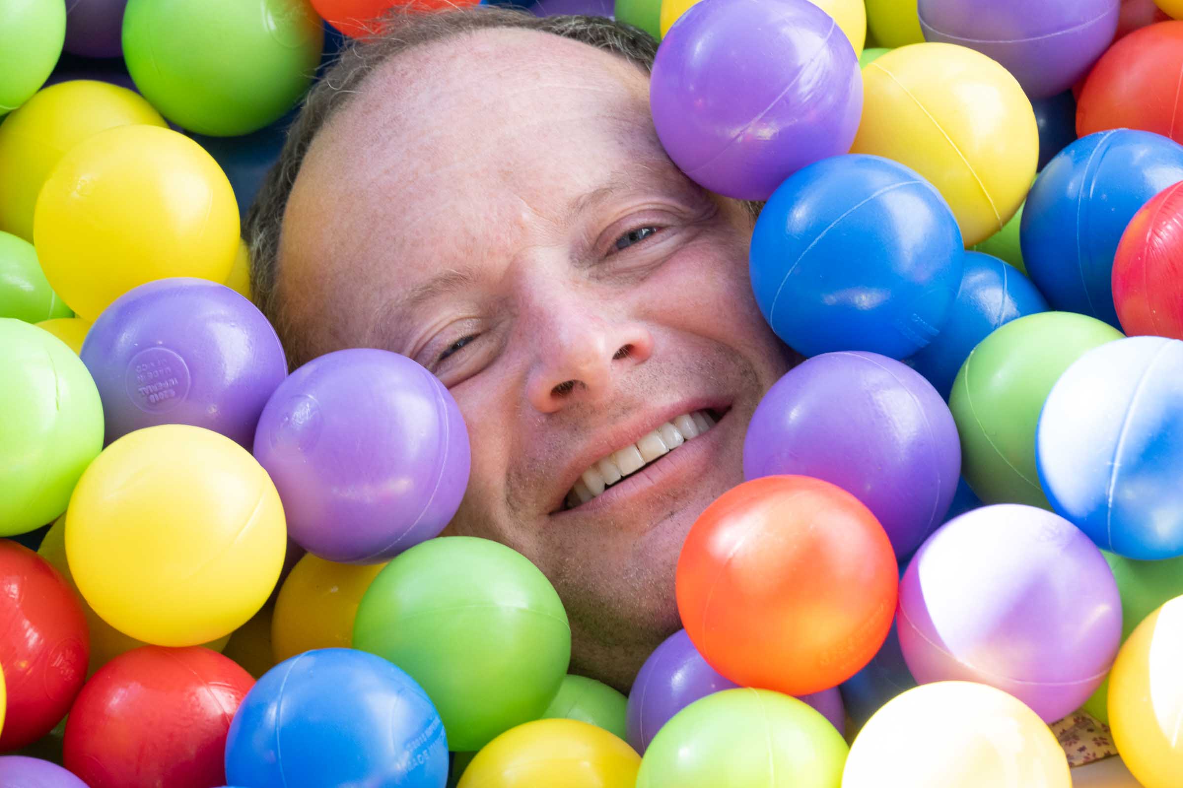 Close-up portrait of a man smiling surrounded by colorful plastic balls in an immersive interactive installation
