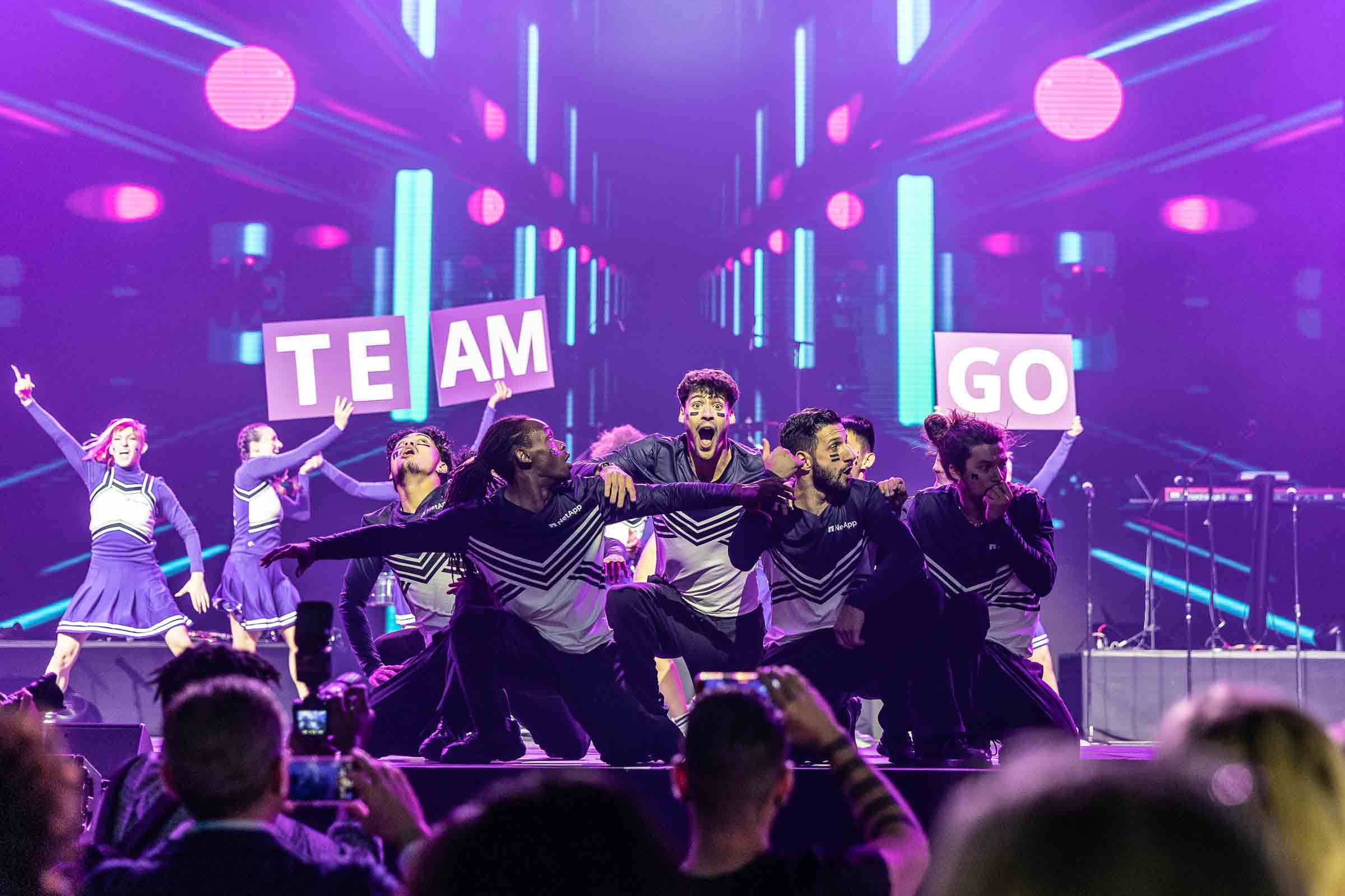 Performers in coordinated costumes dancing on stage with neon lighting design