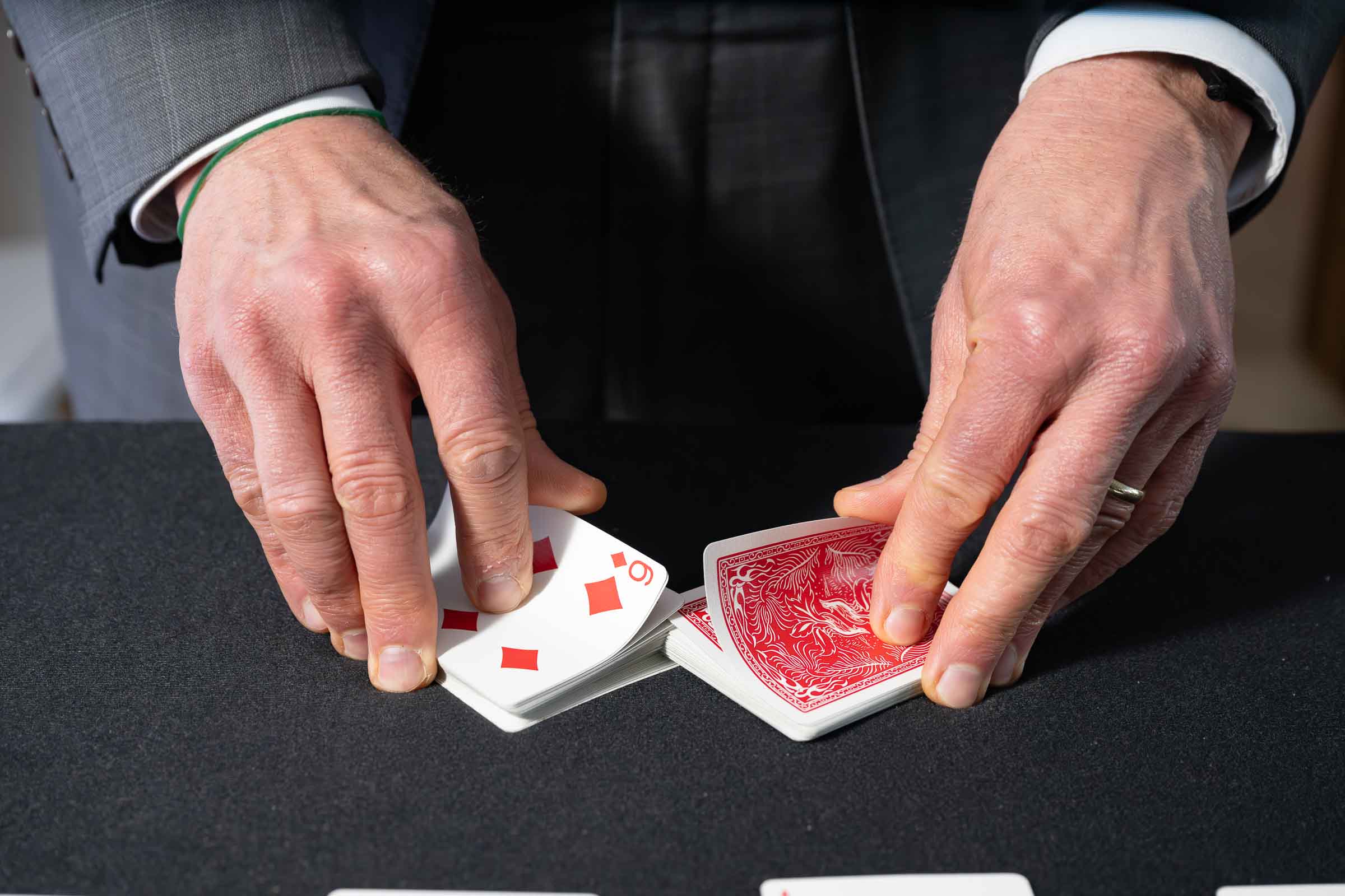 Close-up of a magician's hands performing a card trick on a dark surface during an interactive performance