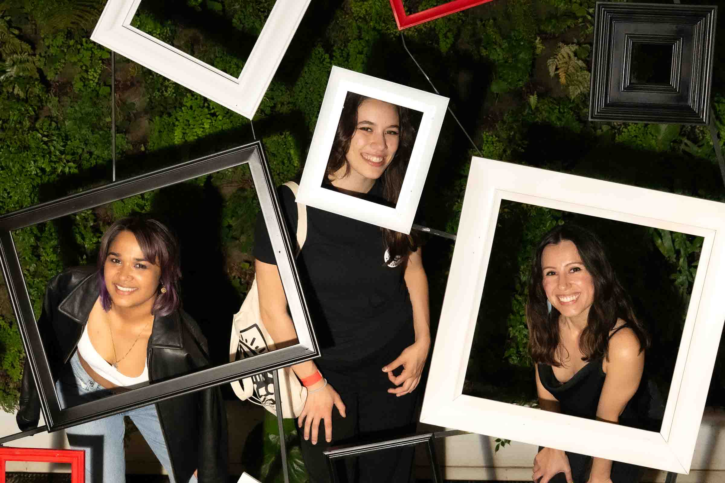 Guests posing with framed photo props at moss-wall interactive installation