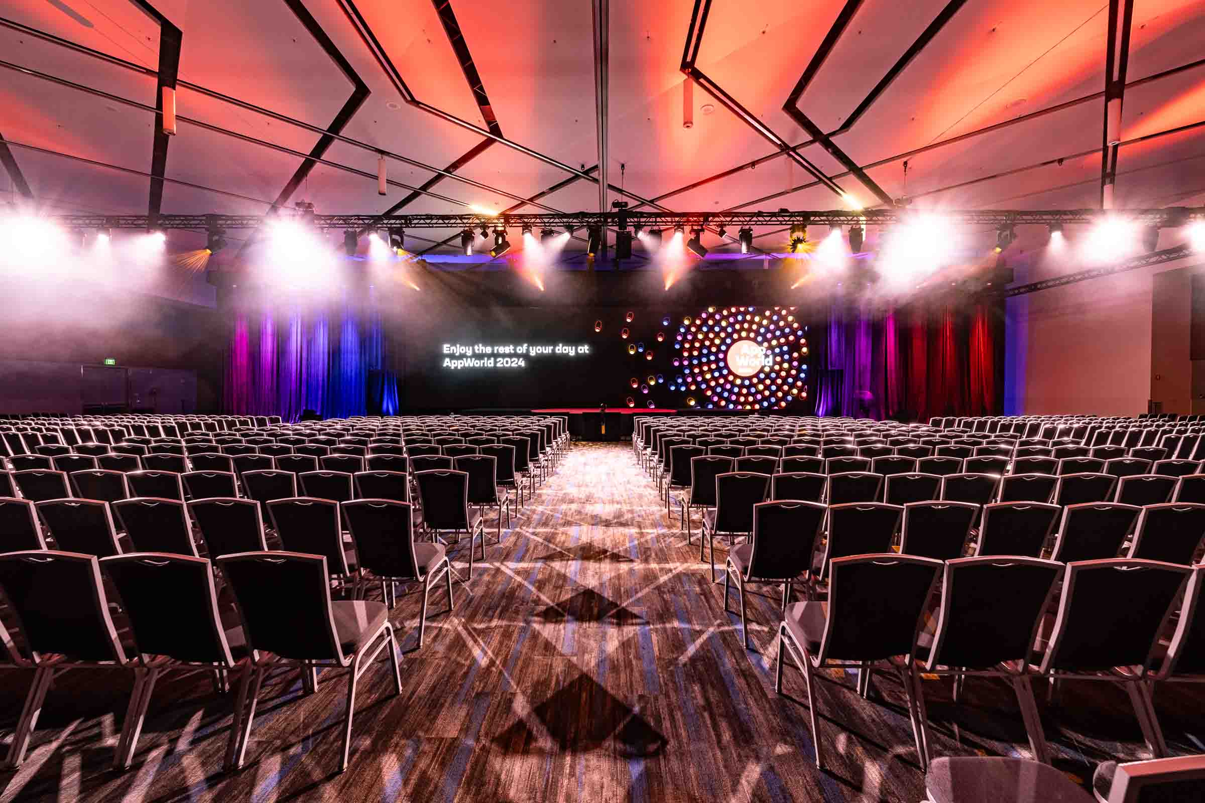 Empty convention center auditorium with rows of black chairs facing stage bathed in red and blue dramatic lighting