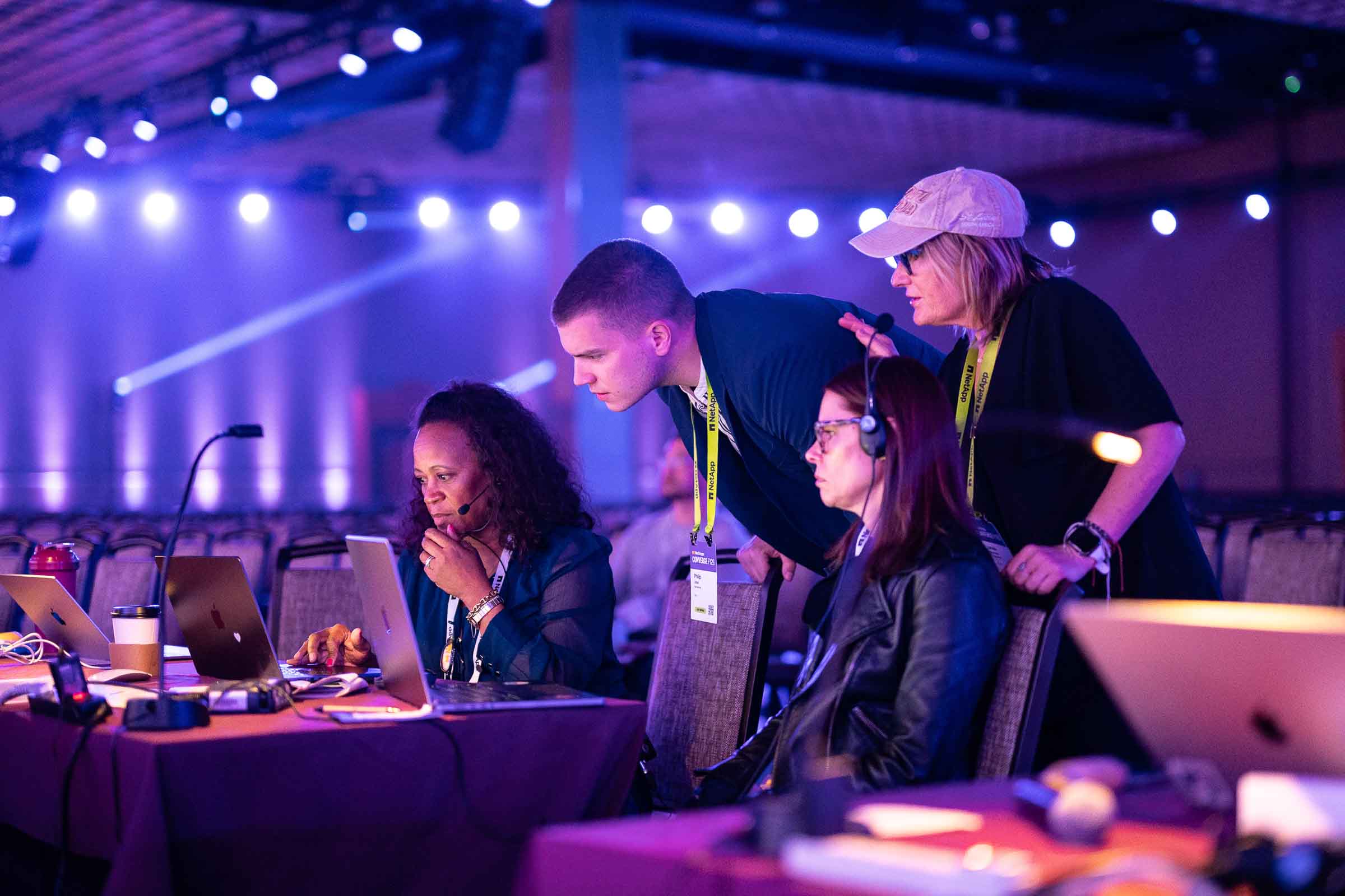 Group of professionals with conference badges gathered at illuminated booth during conference floor event
