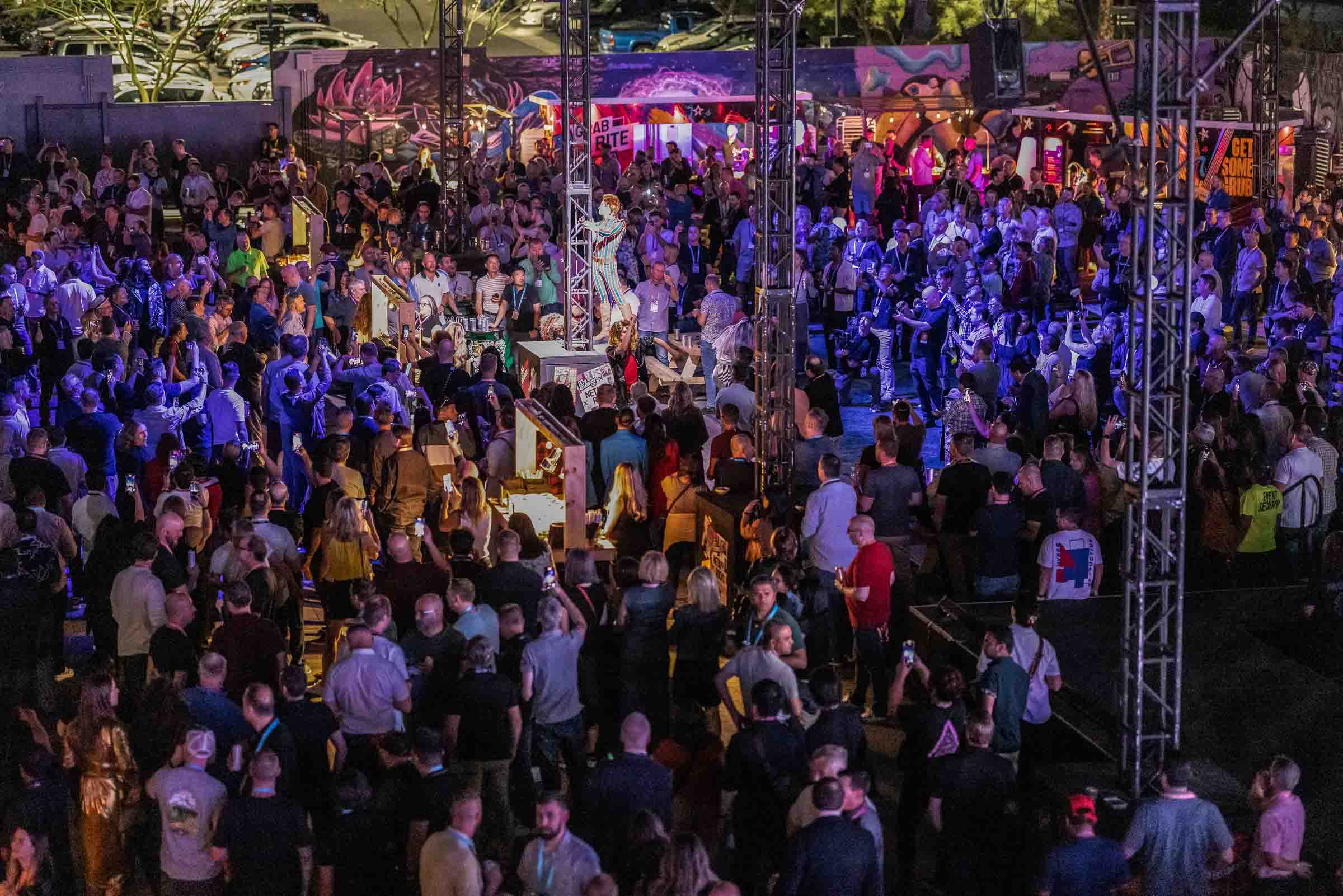 Large outdoor conference stage with attendees and purple-lit entertainment area